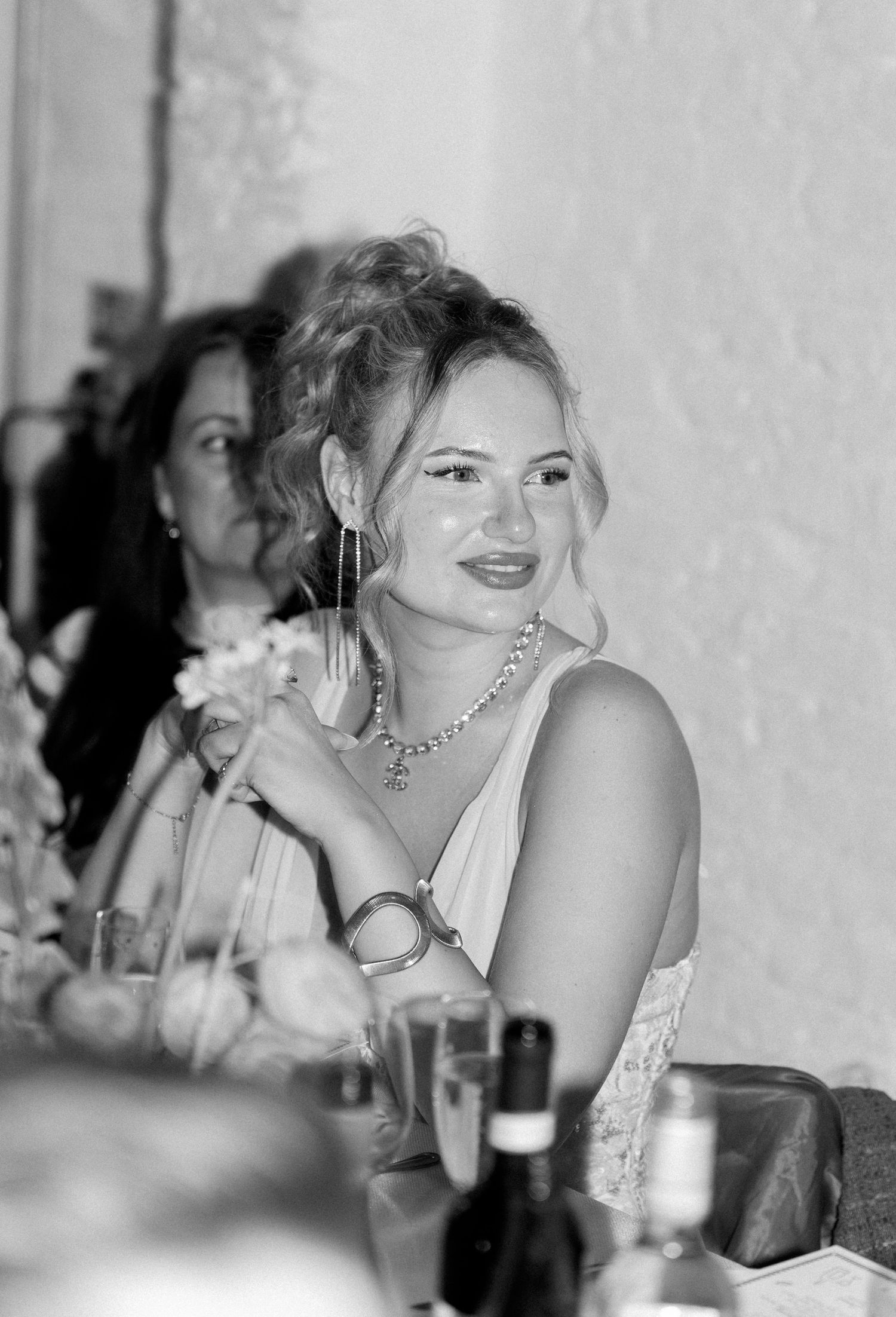 Black and white photo of a guest enjoying a wedding reception with drinks and jewelry.