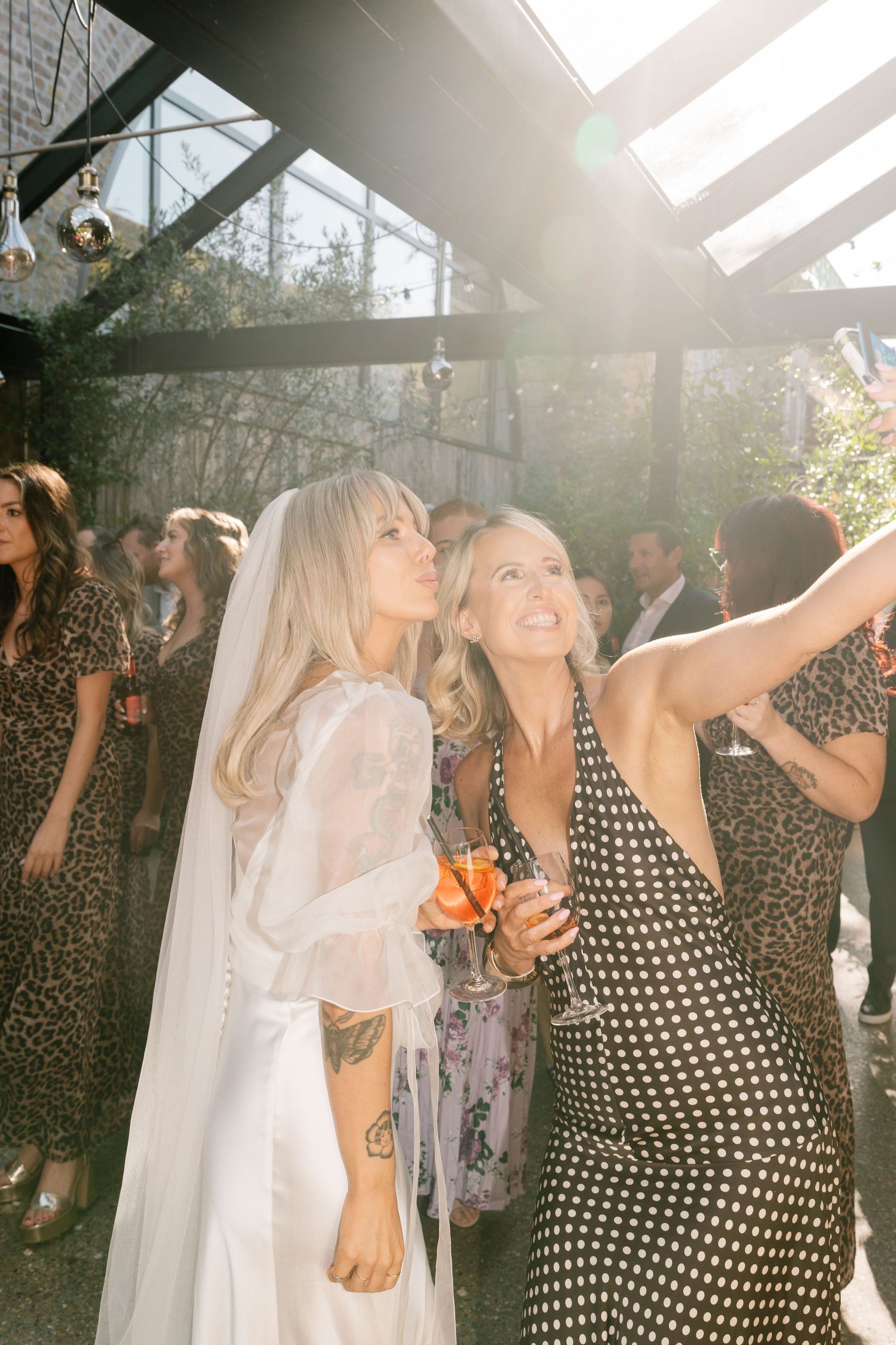 Wedding celebration with guests dancing in sunlit indoor venue.