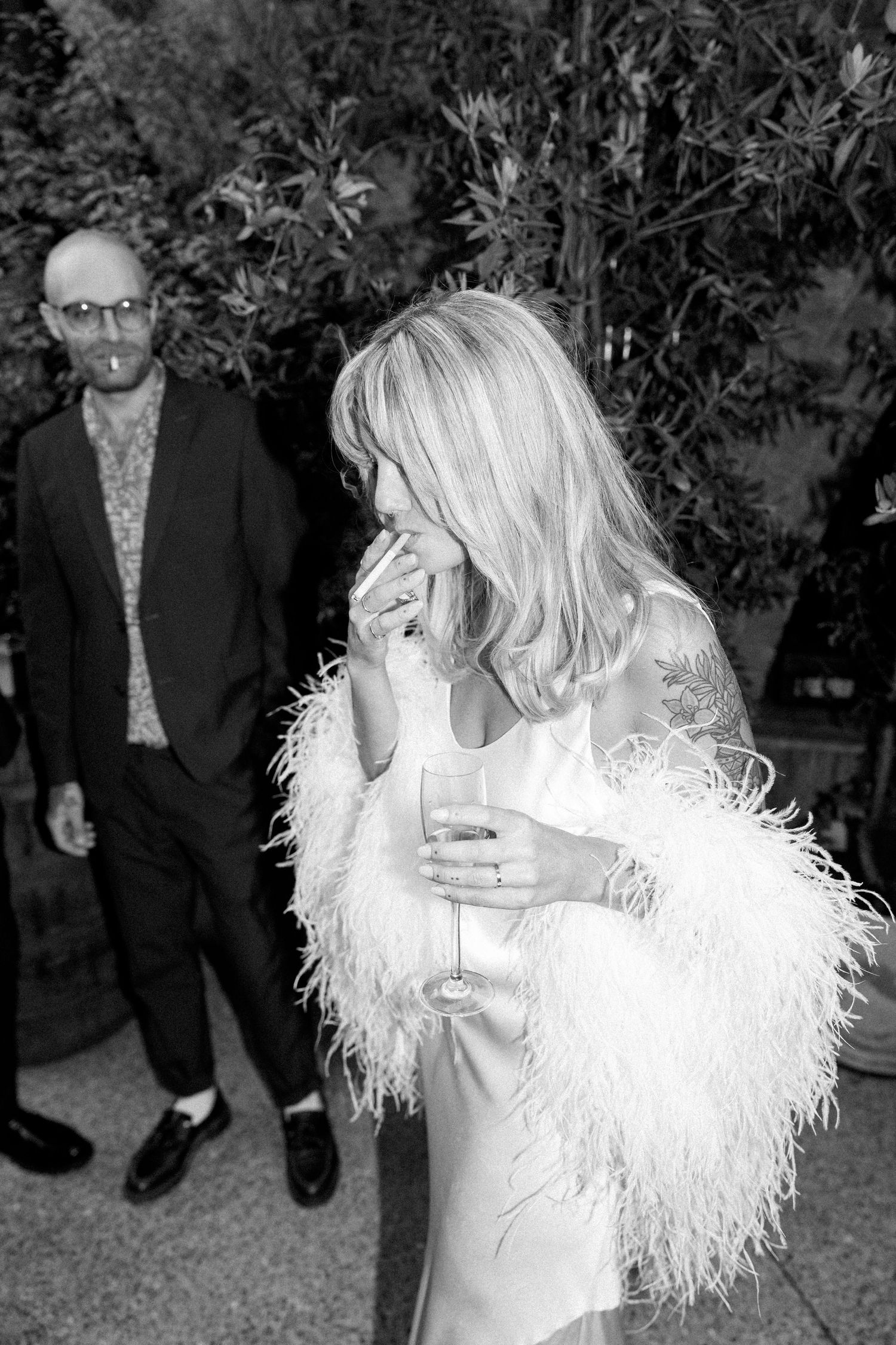 Couple shares romantic moments in a garden setting with white feathered dress details.
