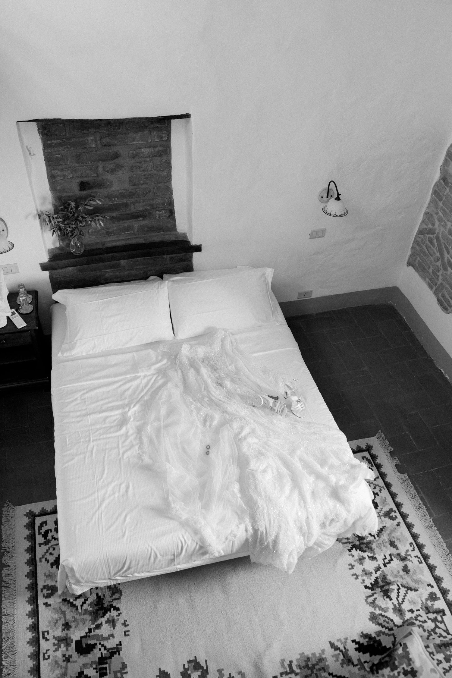 A black and white photo of a wedding dress laid out on a white bed.