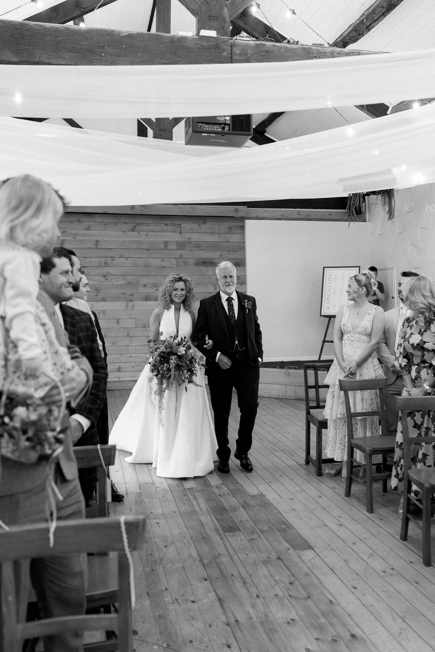Black and white photo of a wedding ceremony setup in a rustic wooden room with chairs.