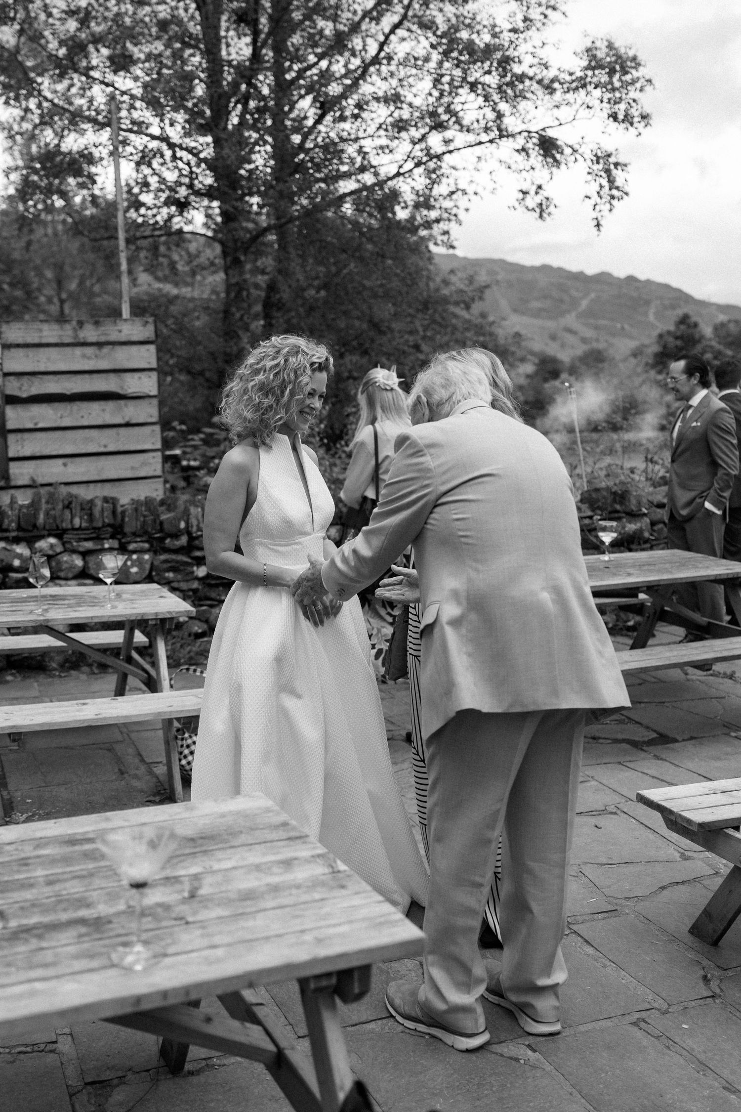 Black and white photo of guests mingling on an outdoor patio with picnic tables and mountain views.