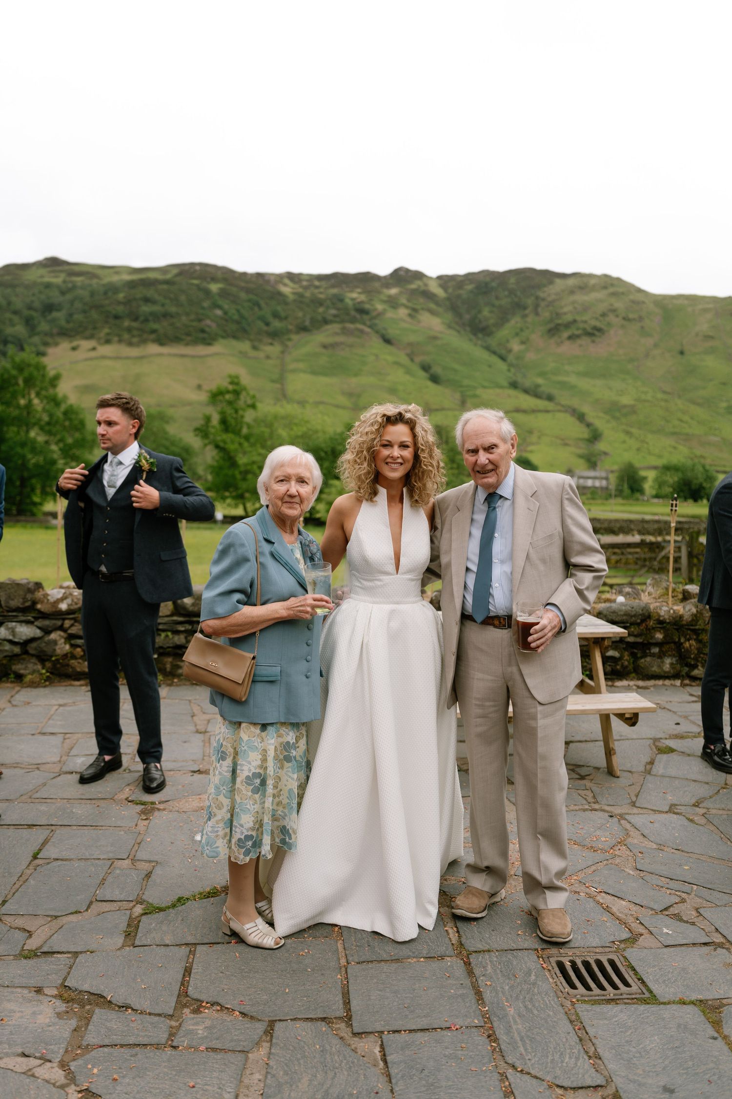 Wedding party members walk across a stone patio with scenic mountains in the background.