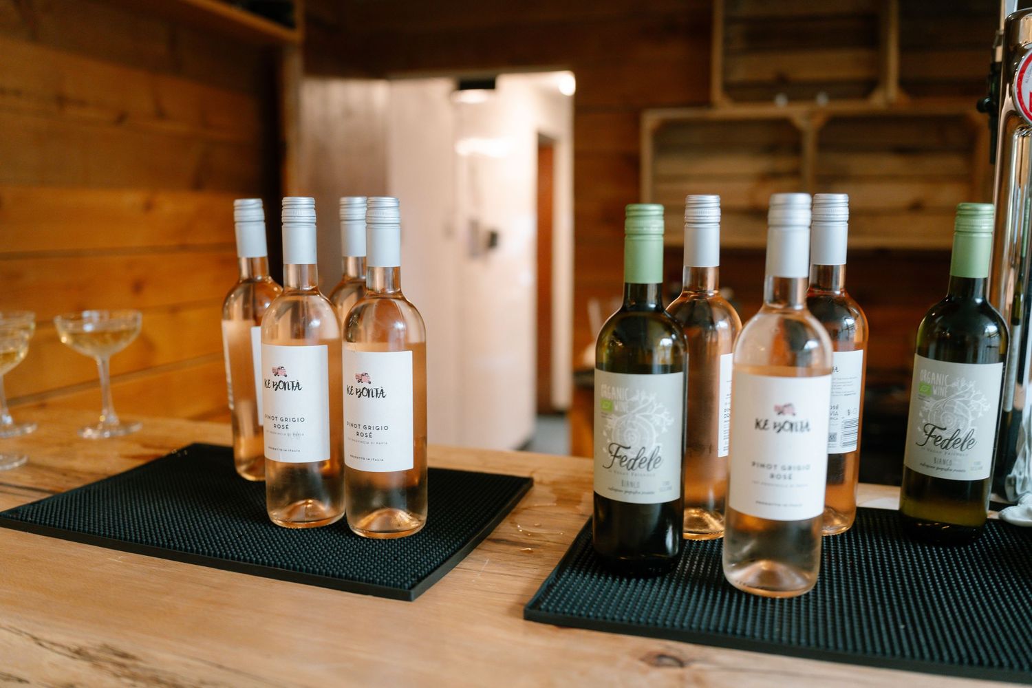 Wine bottles lined up on a wooden surface with empty glasses.