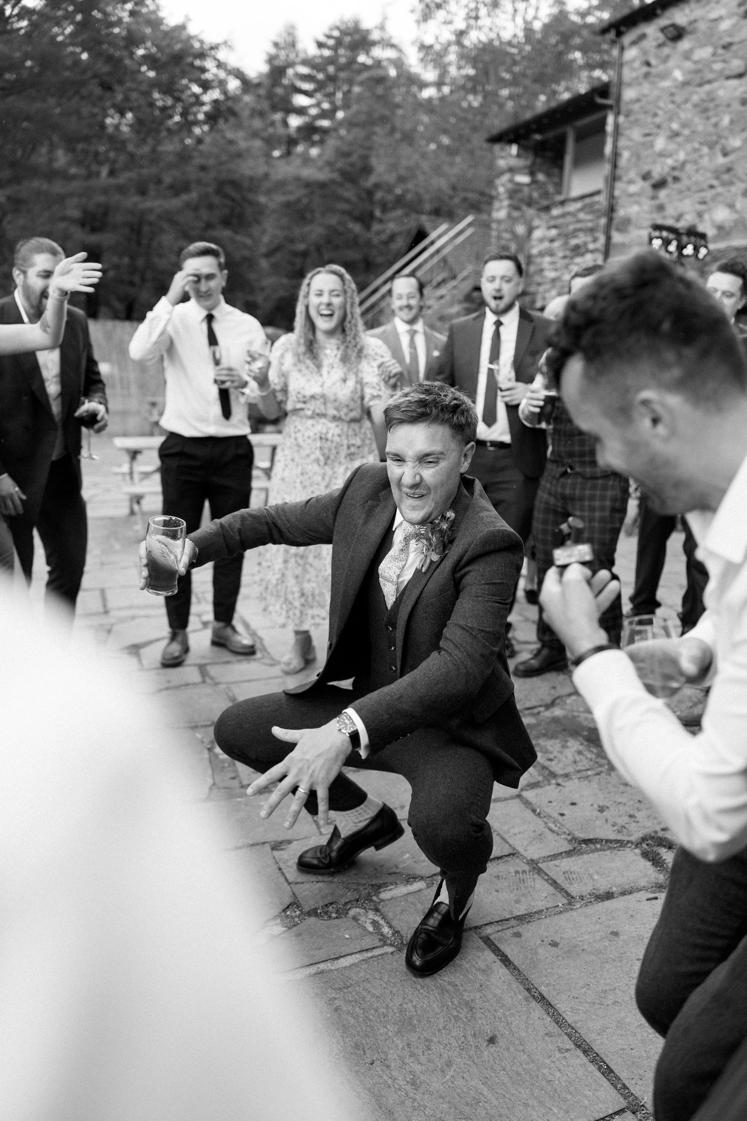 Wedding party members performing energetic dance moves on stone patio.