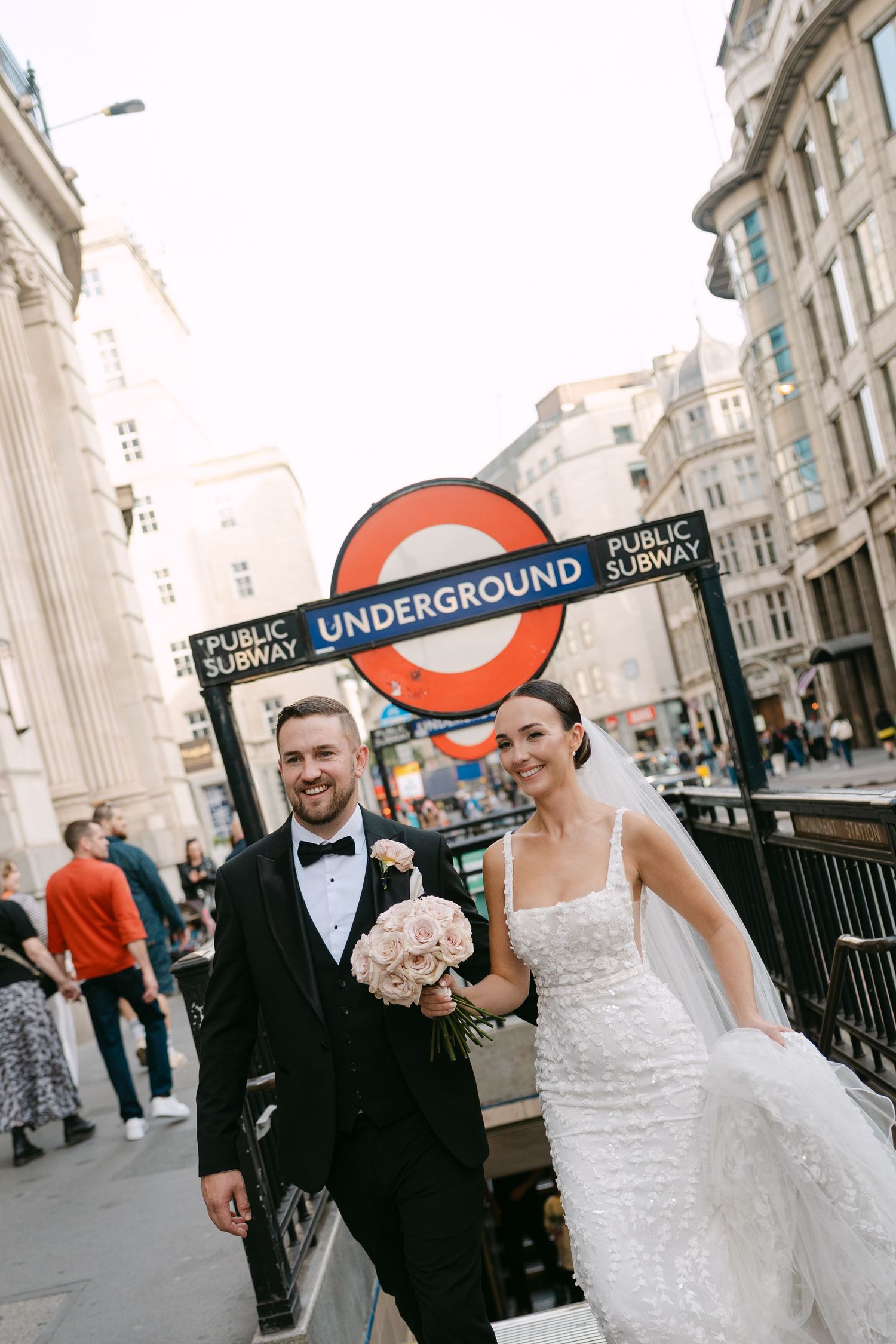 Wedding couple near London Underground sign entrance in formal attire.