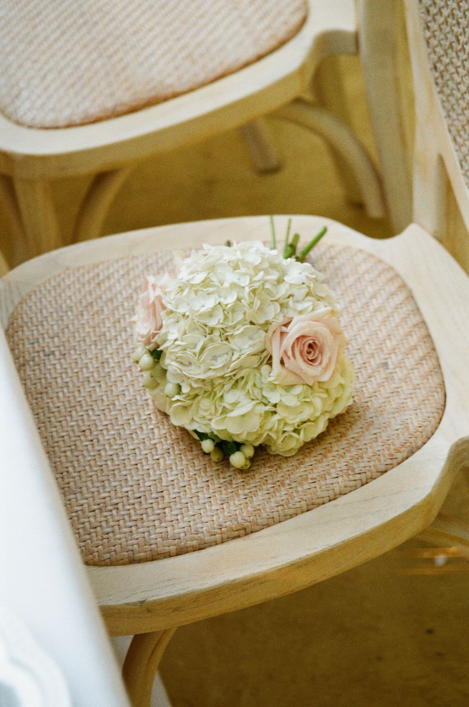 Delicate hydrangea and rose bouquets placed on natural burlap chairs for wedding decor.
