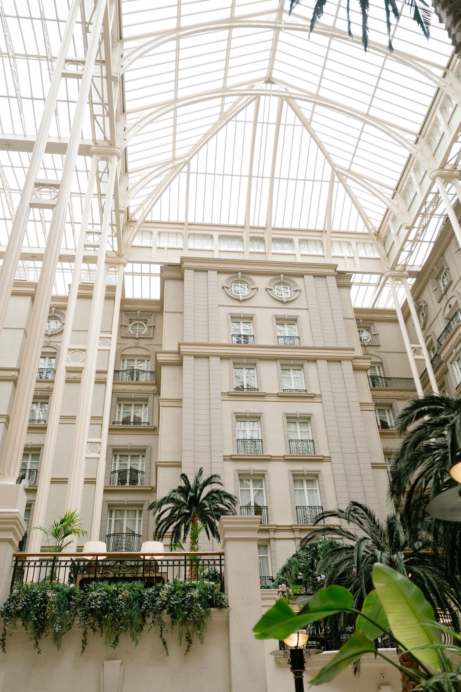 Interior atrium of a luxury hotel with soaring glass ceiling and palm trees.