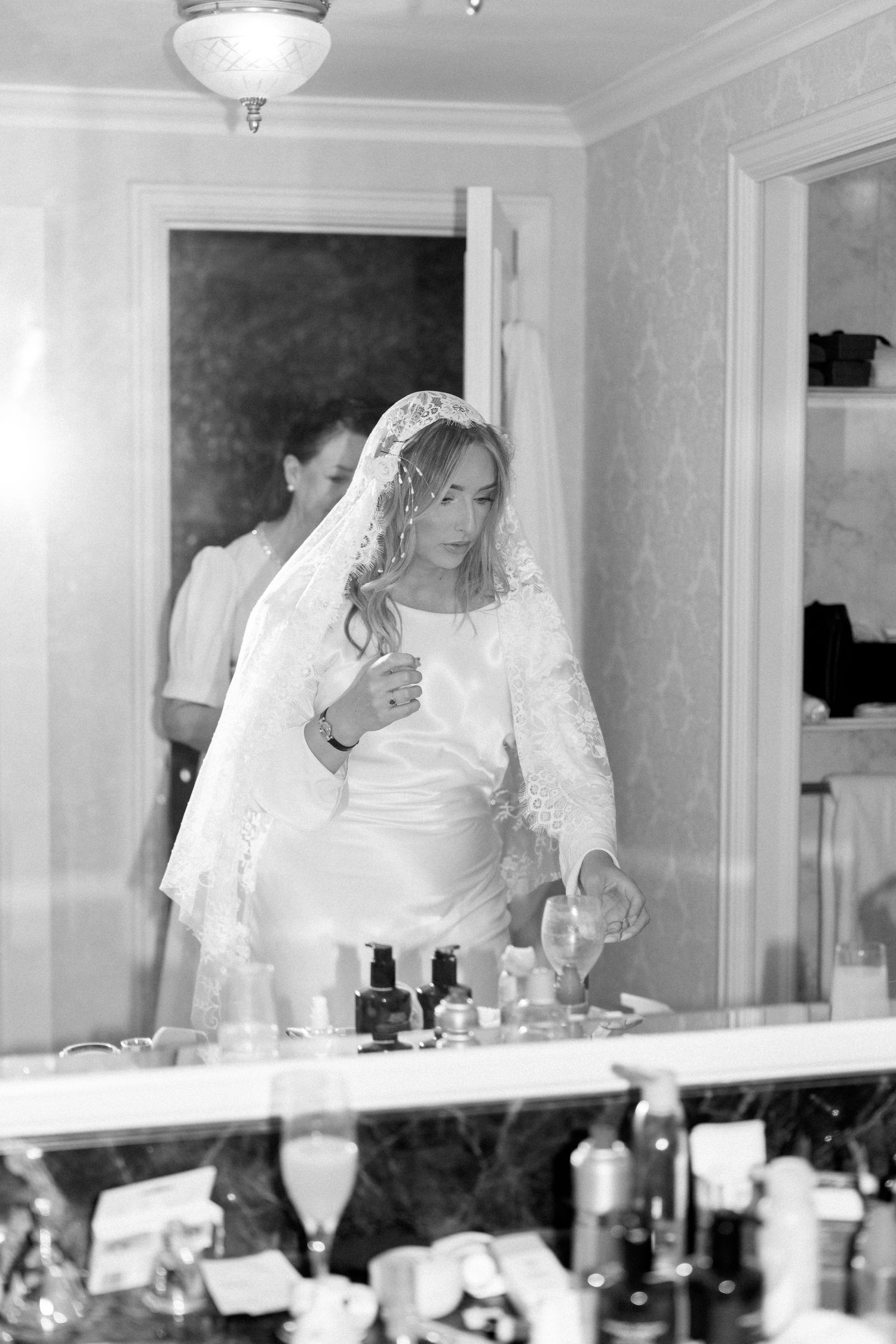 Bridal party getting ready in front of elegant vanity mirrors in a white room.