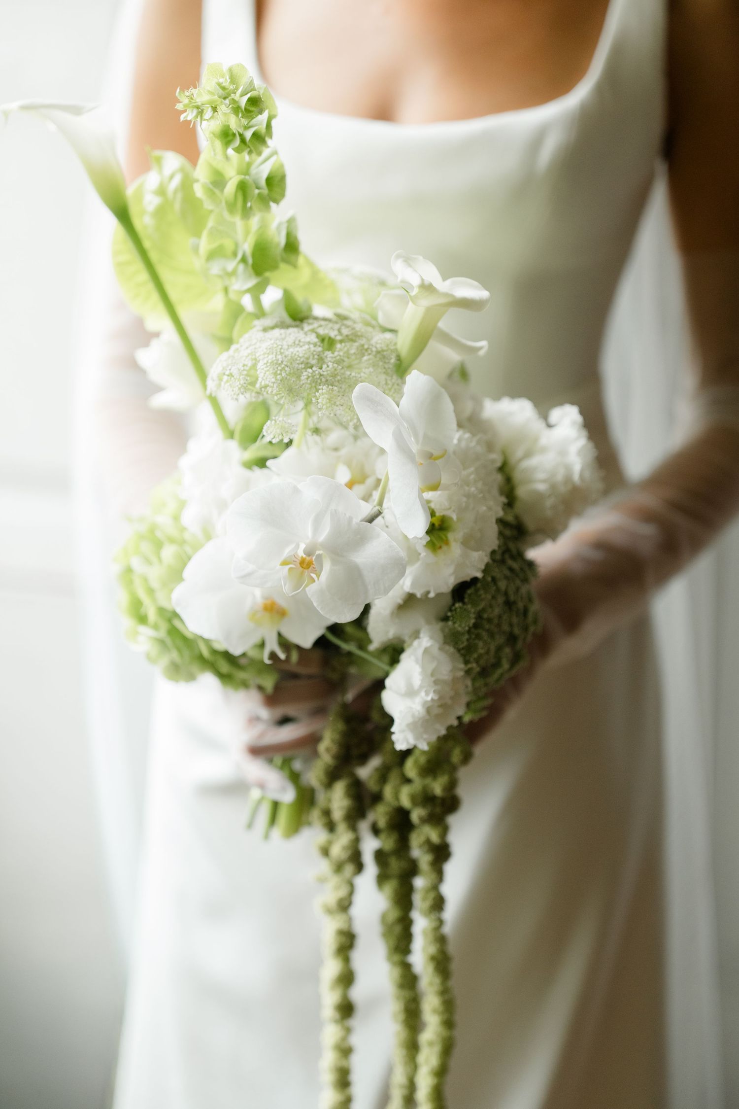 Close-up of bridal bouquet with white orchids, peonies and green trailing amaranthus.