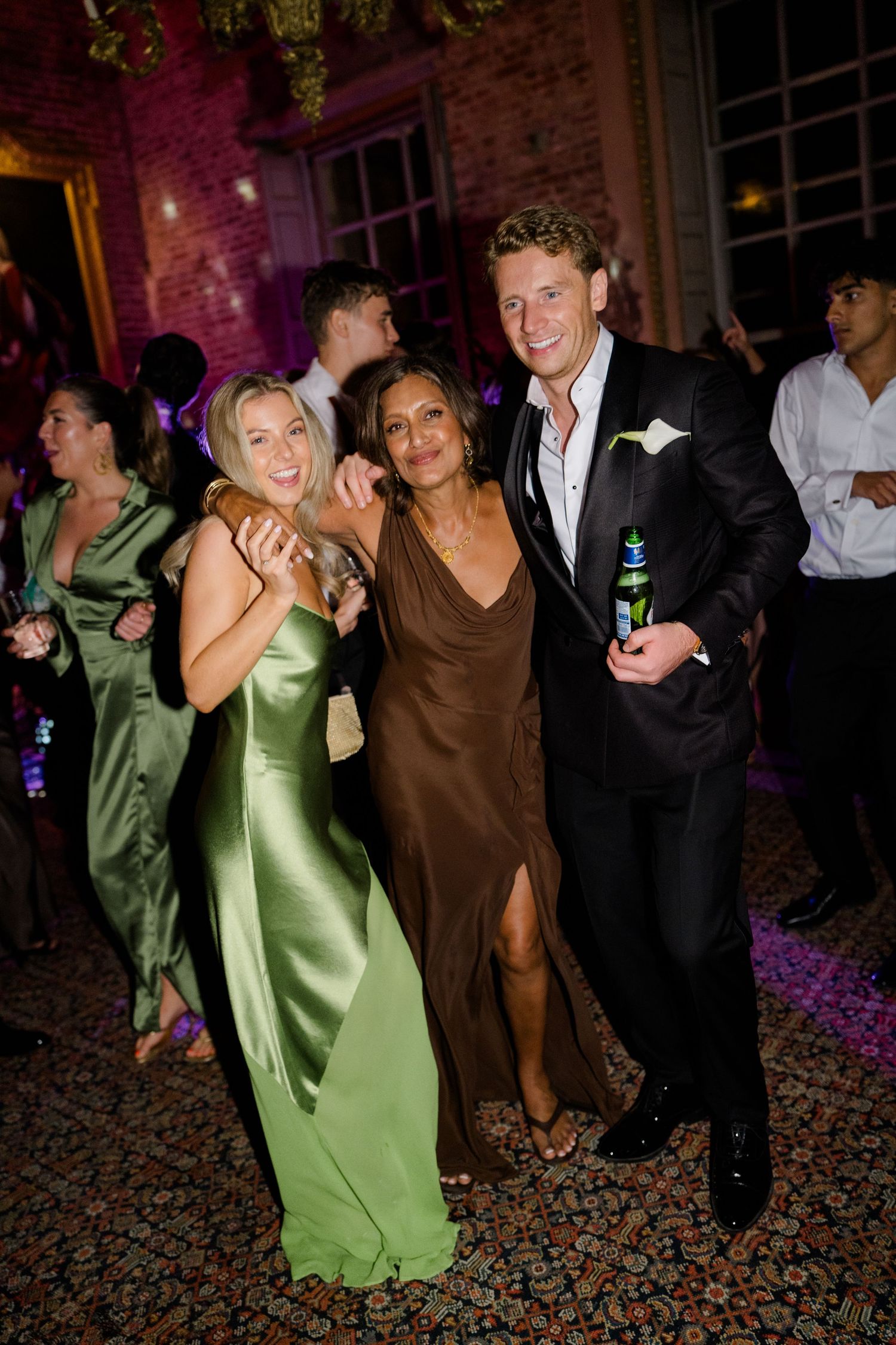 Three wedding guests smile and pose together on dance floor at elegant evening reception.