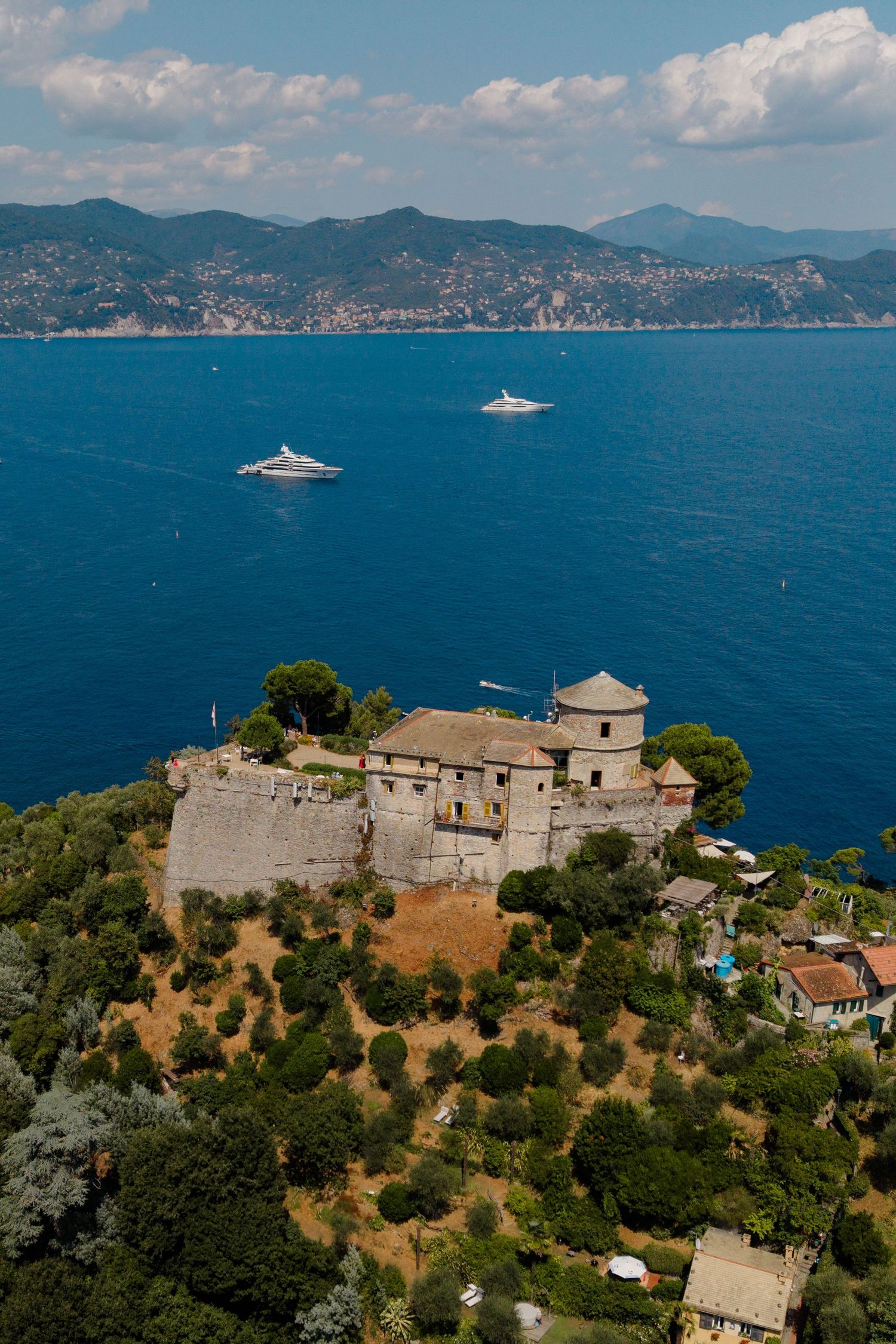 Aerial view of historic Castello Brown fortress on hilltop overlooking deep blue Ligurian Sea.