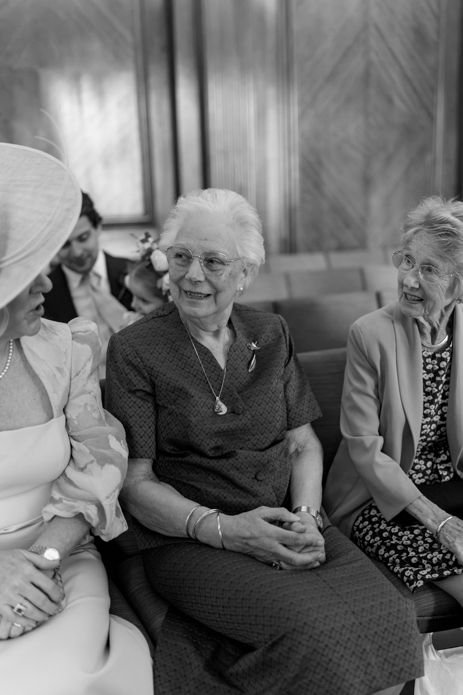 Black and white photo of elderly women smiling and chatting at a wedding reception venue.