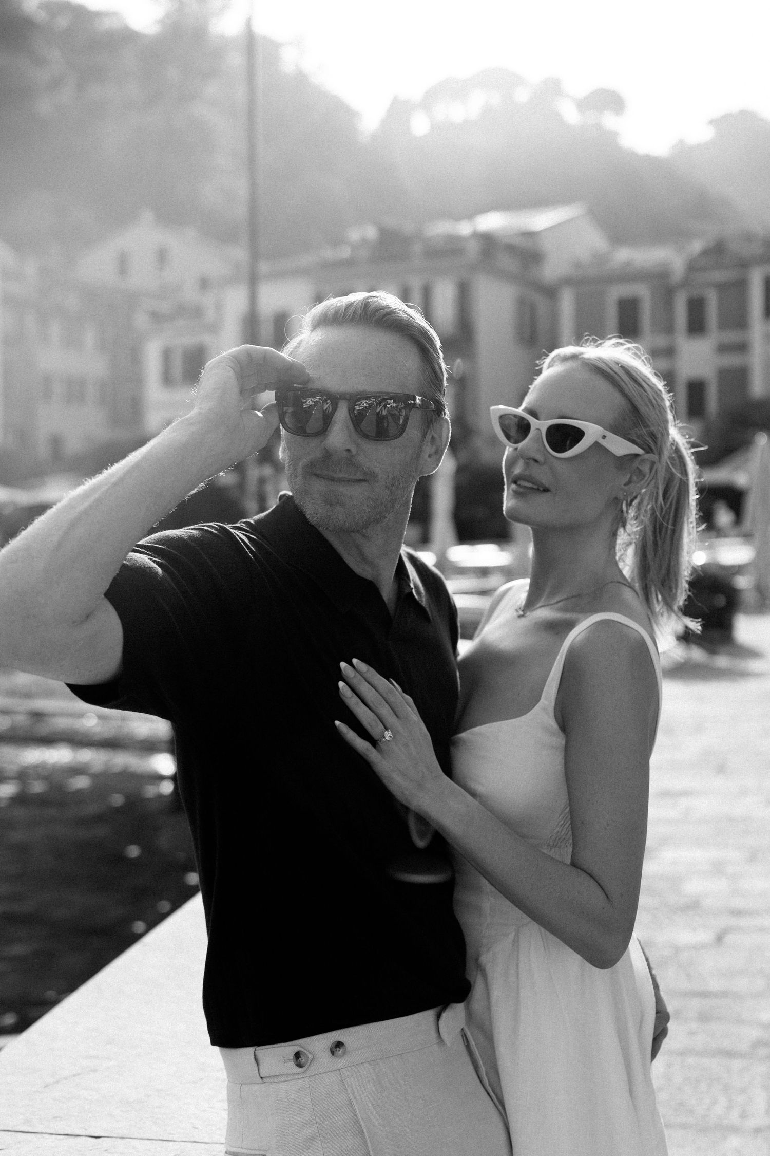 Black and white photo of a stylish couple wearing sunglasses posing together in the scenic village of Portofino, Italy.