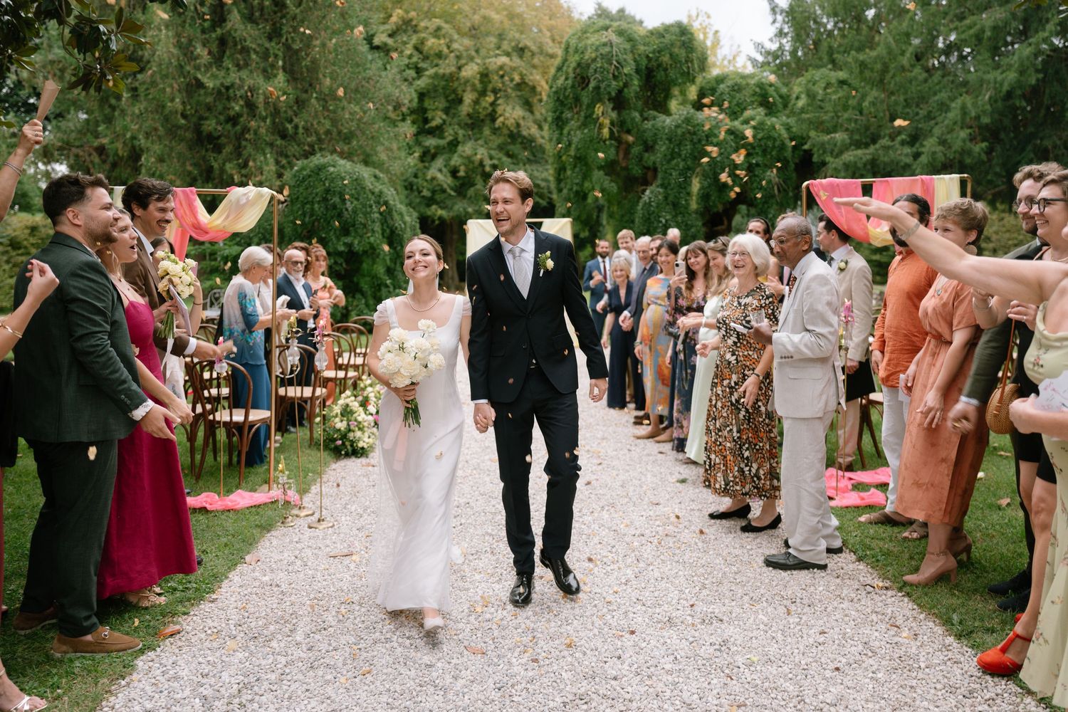Wedding guests line a gravel path cheering as the newlyweds make their celebratory exit.