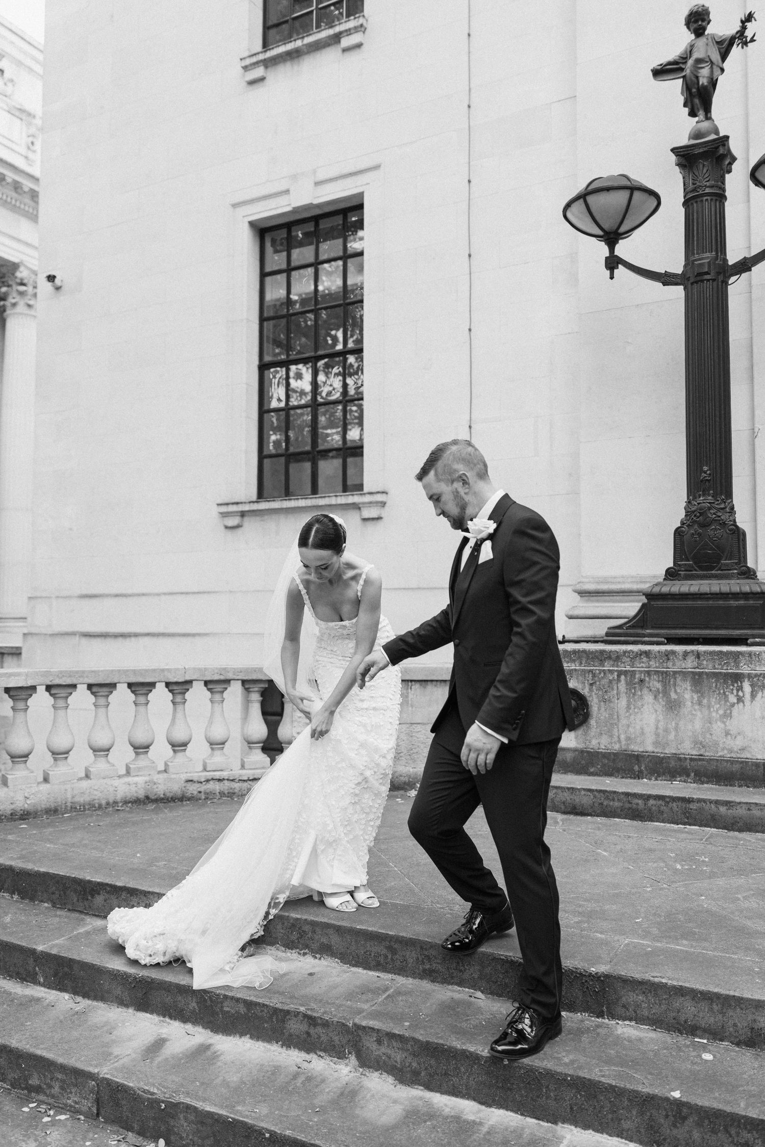 Wedding couple ascending stone steps outside historic building.