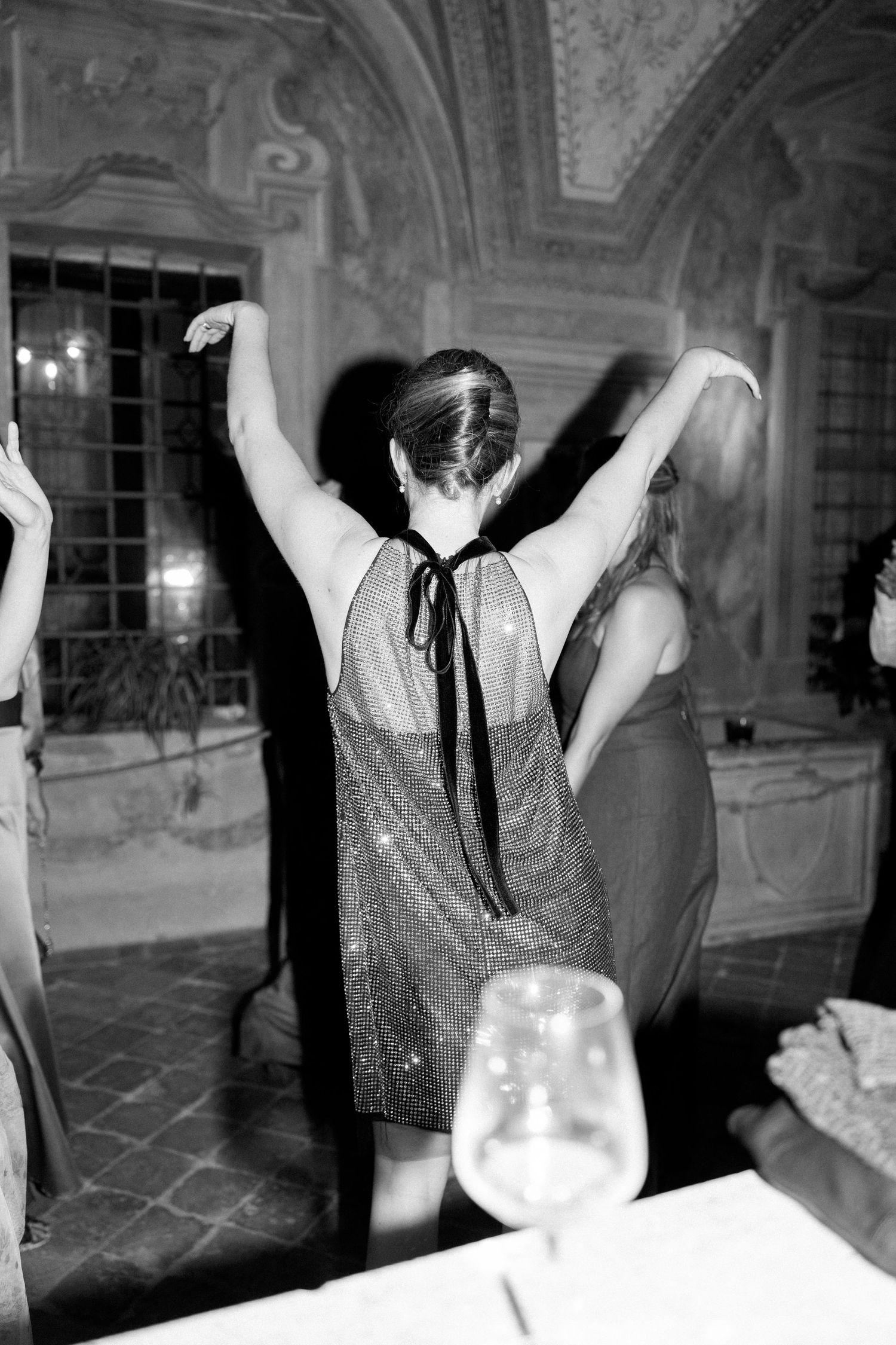 Person in sparkly dress dancing with raised arms in a grand ballroom setting.
