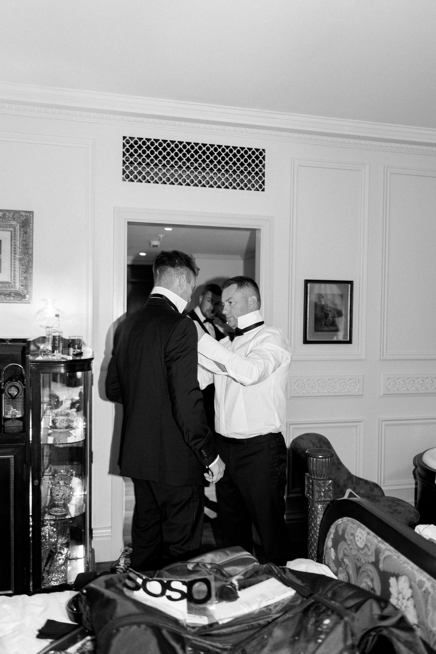 Two people in formal attire help each other prepare in a hotel room.