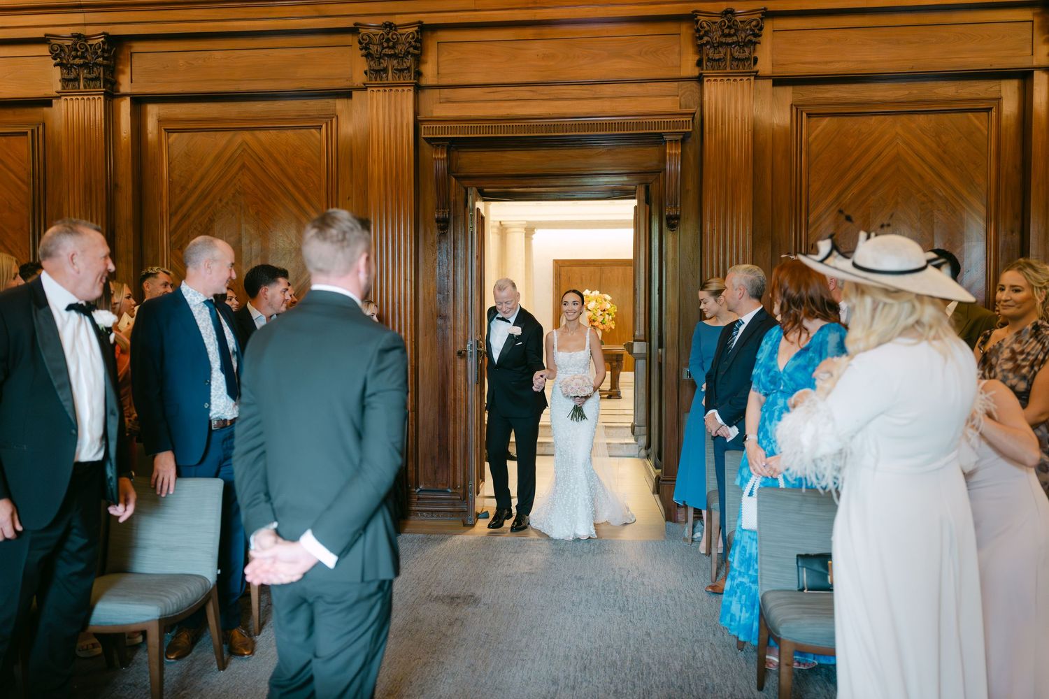 Wedding party members gather in an elegant wood-paneled venue with ornate architectural details.