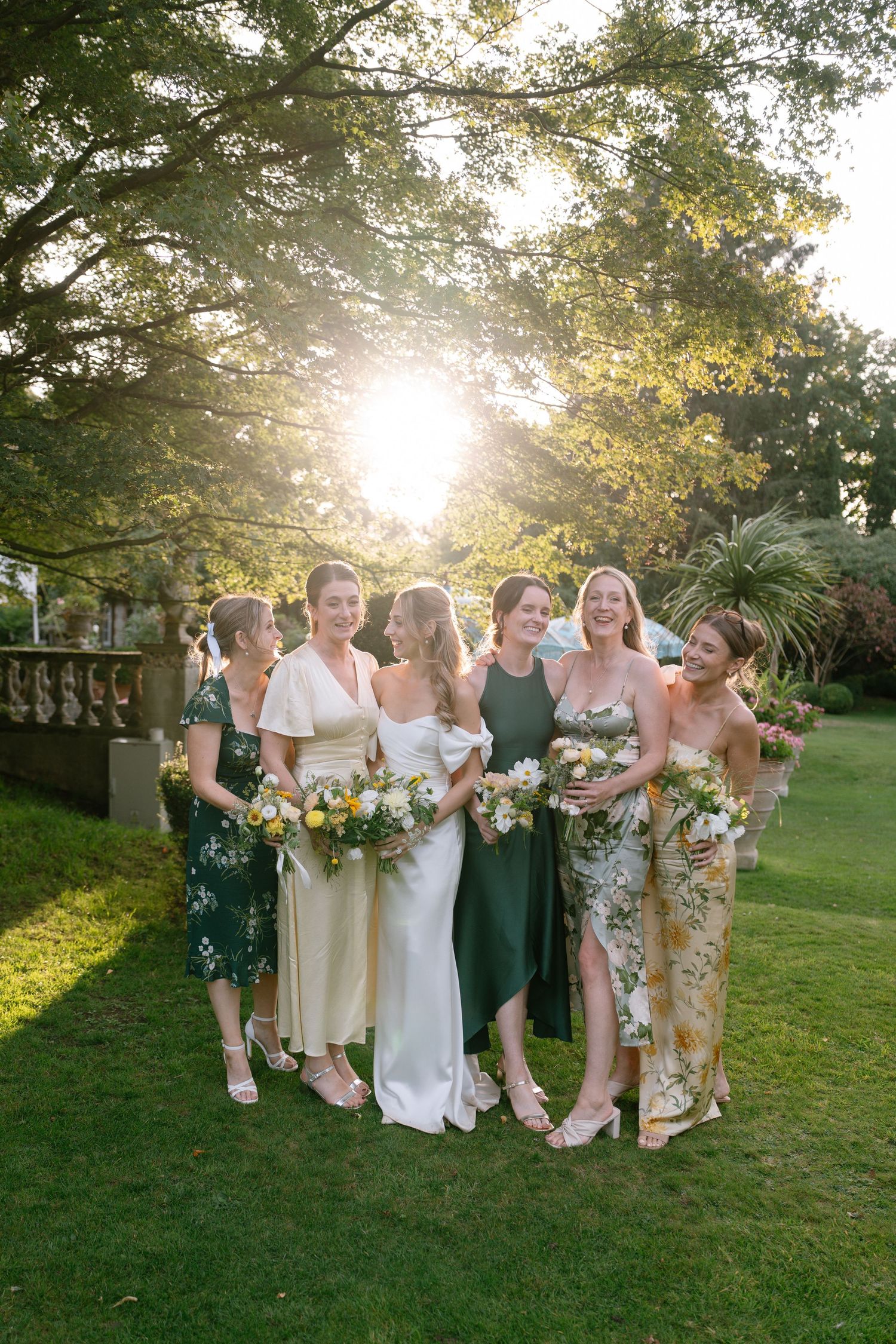 Wedding party poses together on a sunlit garden lawn during golden hour.