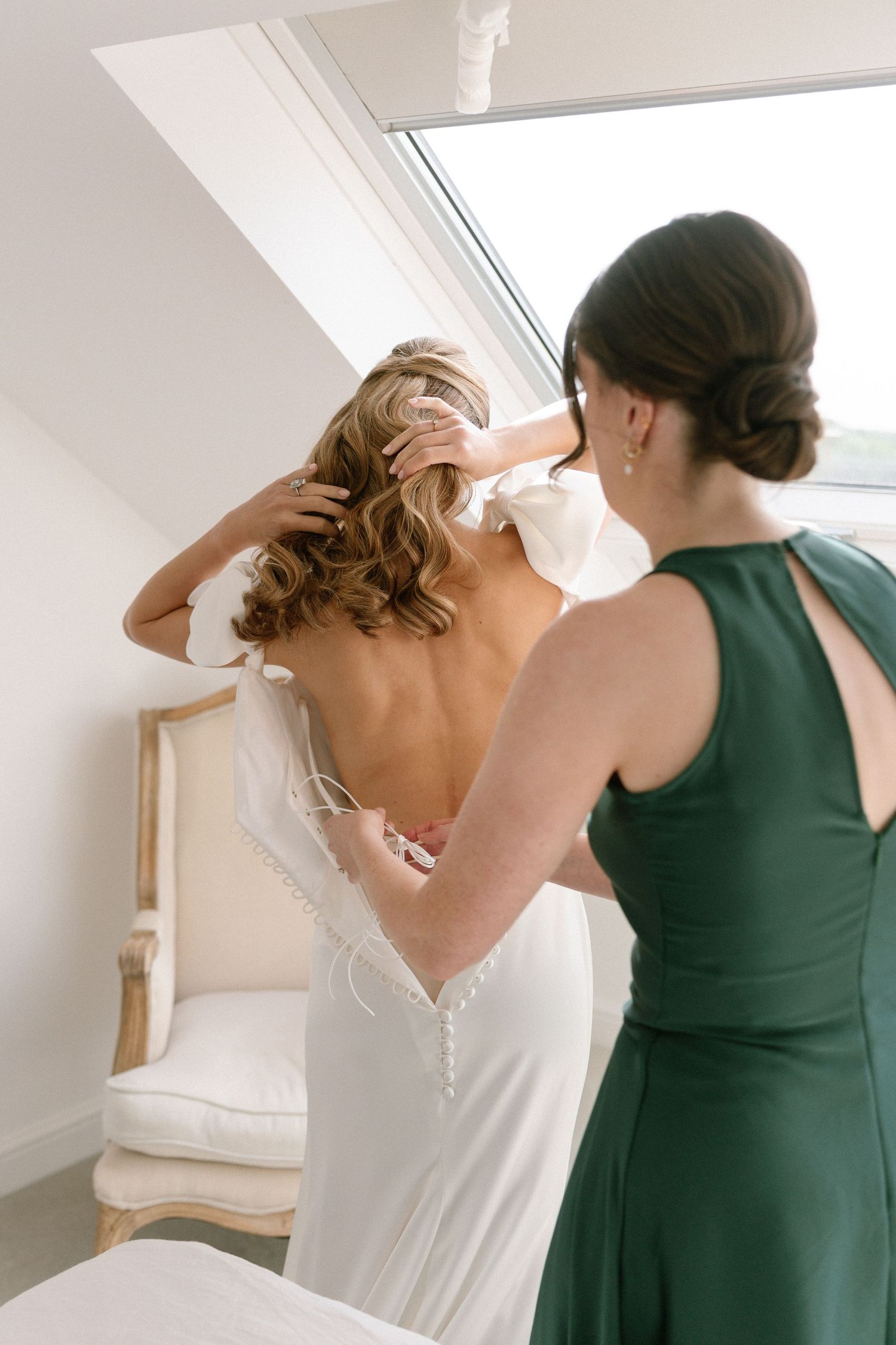 Two women in contrasting dresses preparing in a bright attic room.