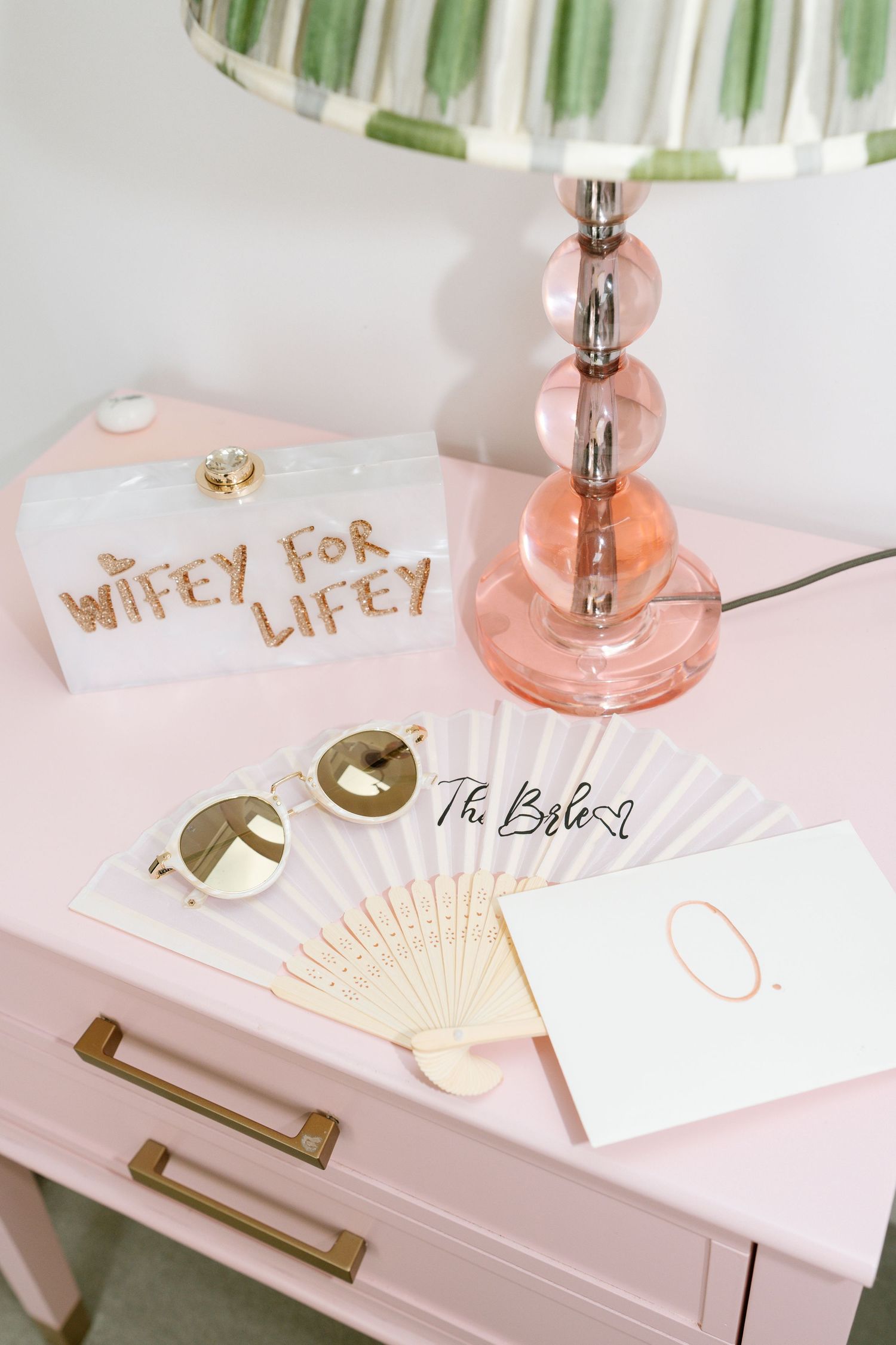 Pink vanity with decorative lamp, fan, and gold text details for wedding preparation.