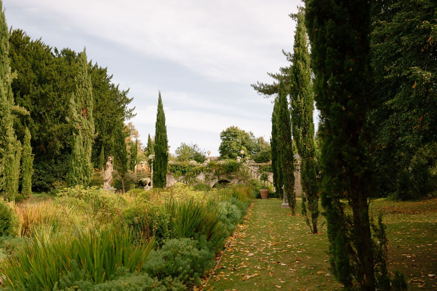 Scenic garden pathway lined with tall cypress trees and lush greenery on a sunny day.