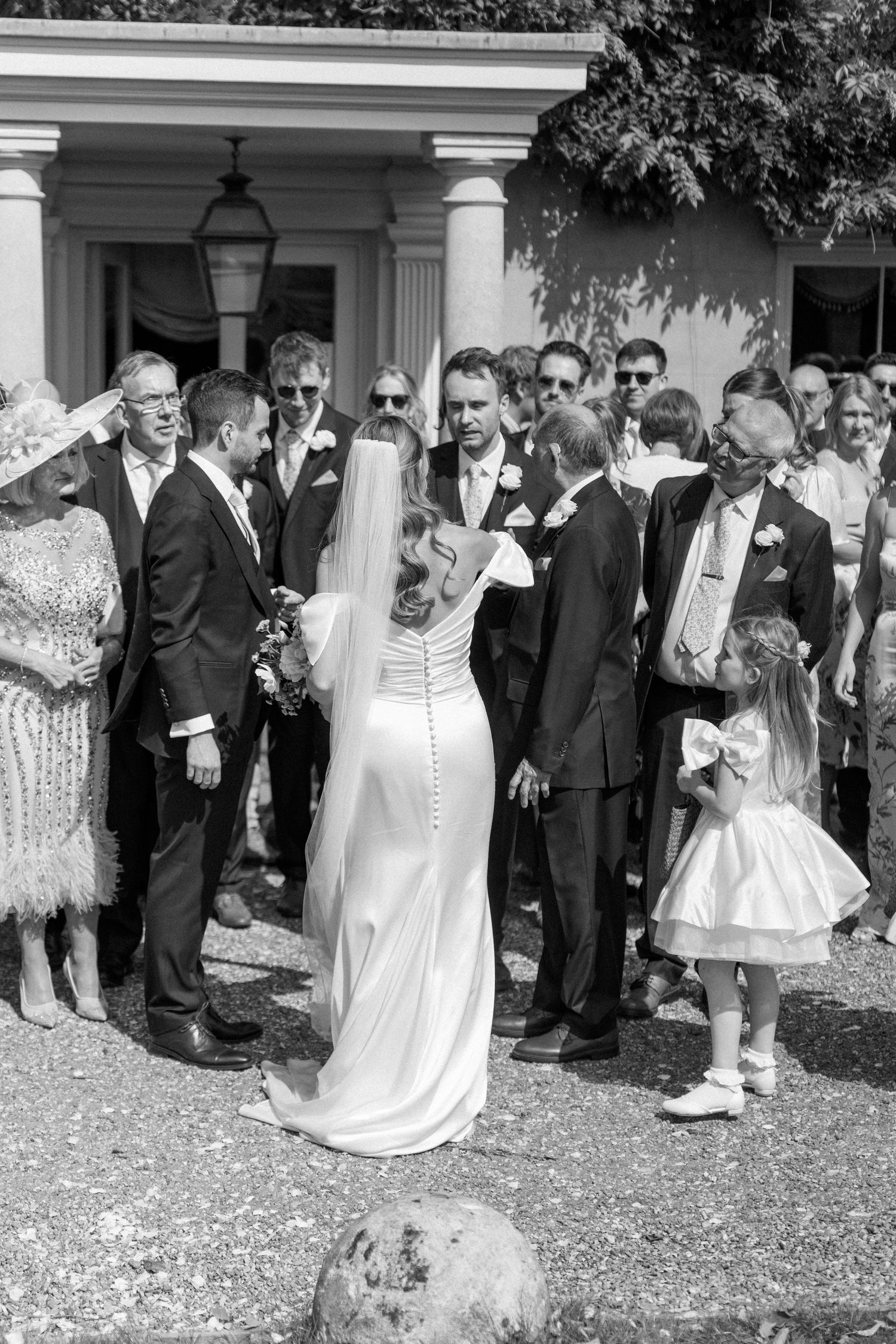Black and white image of wedding party celebrating with guests outside historic venue.