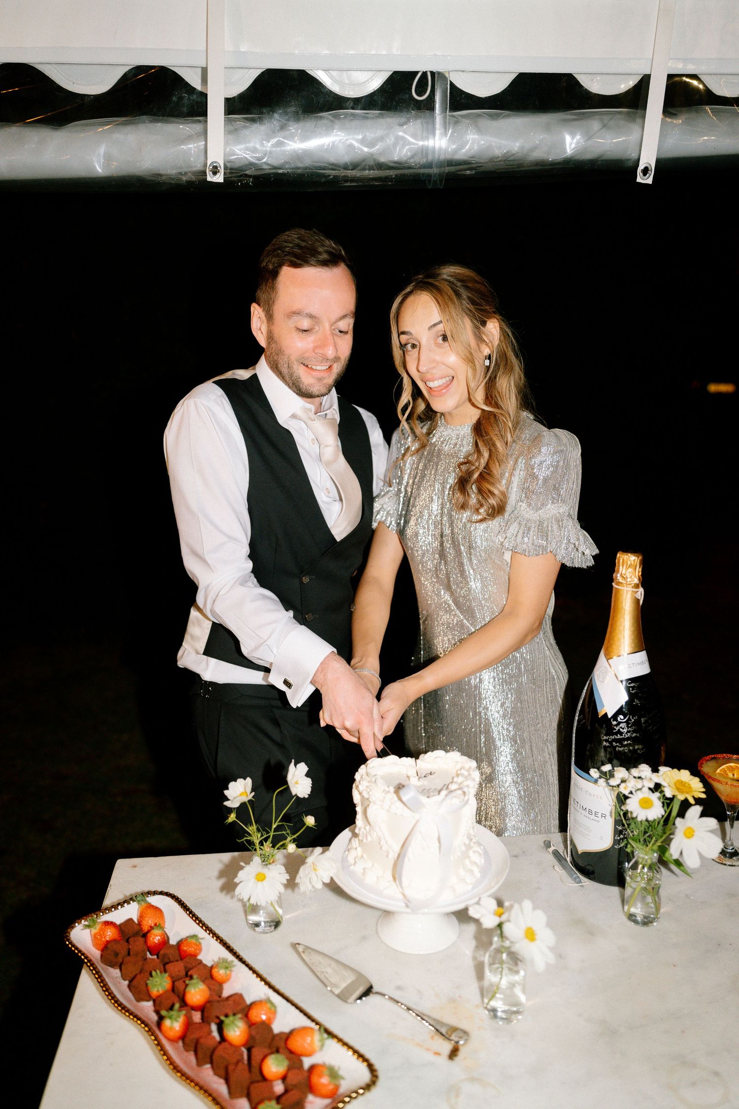 A couple in formal attire share an intimate moment at a reception table with champagne and desserts.