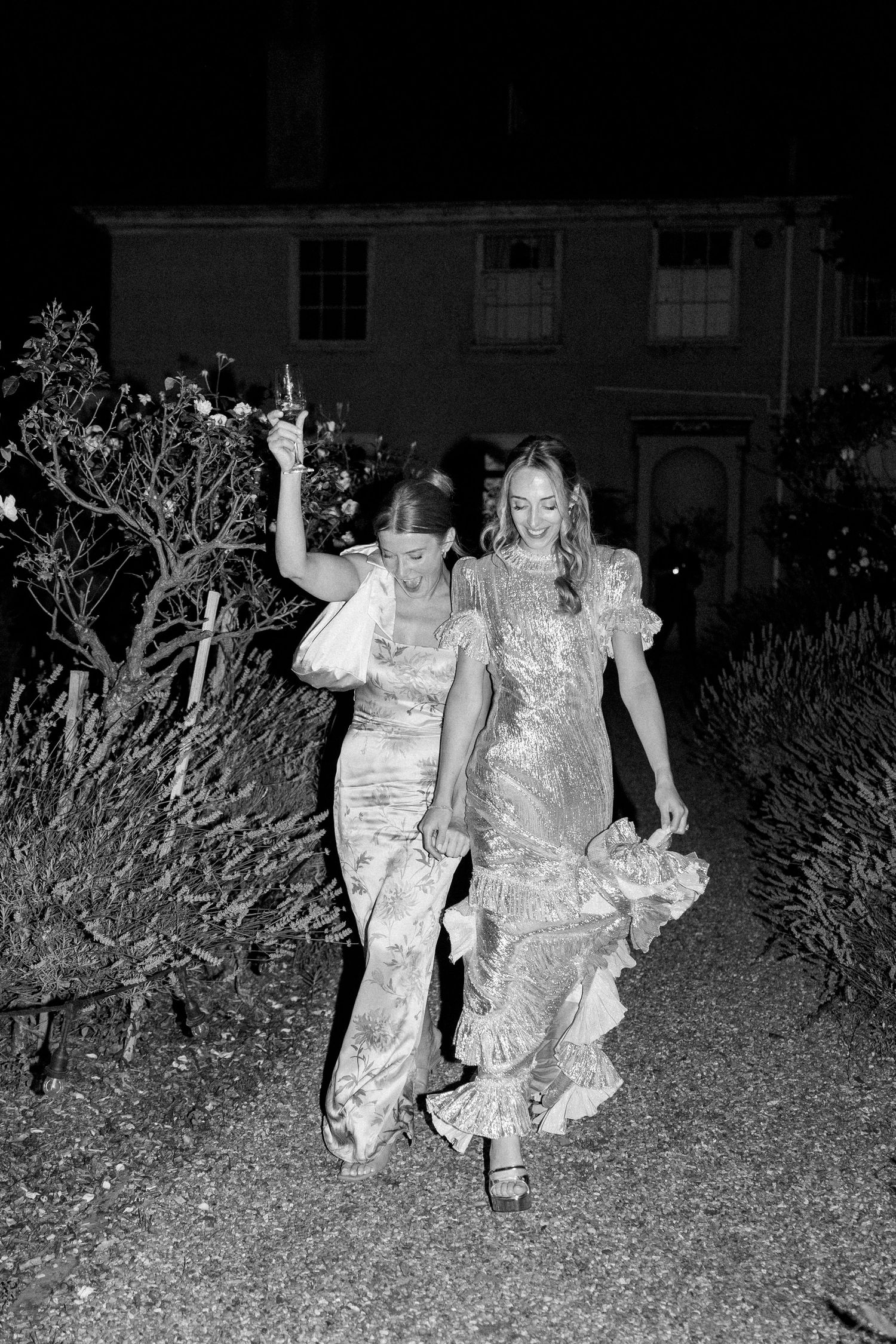 Night time photo of party guests walking through garden path in formal wear.