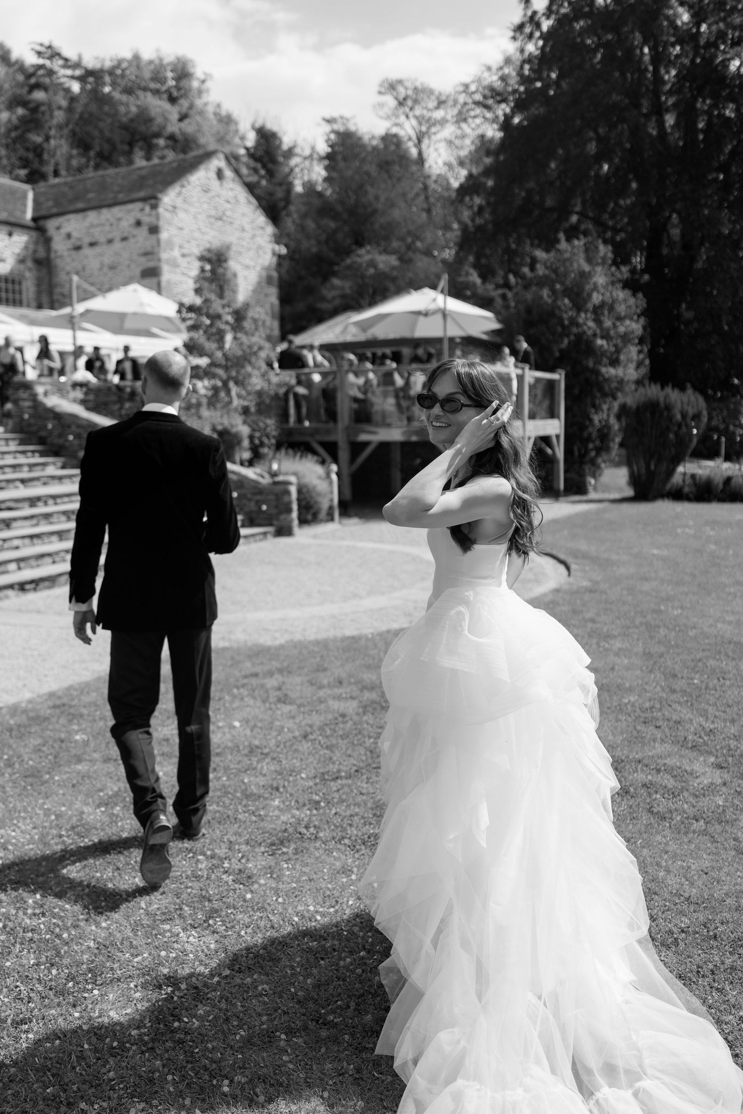 A couple in wedding attire walks across an outdoor venue with tents in the background.