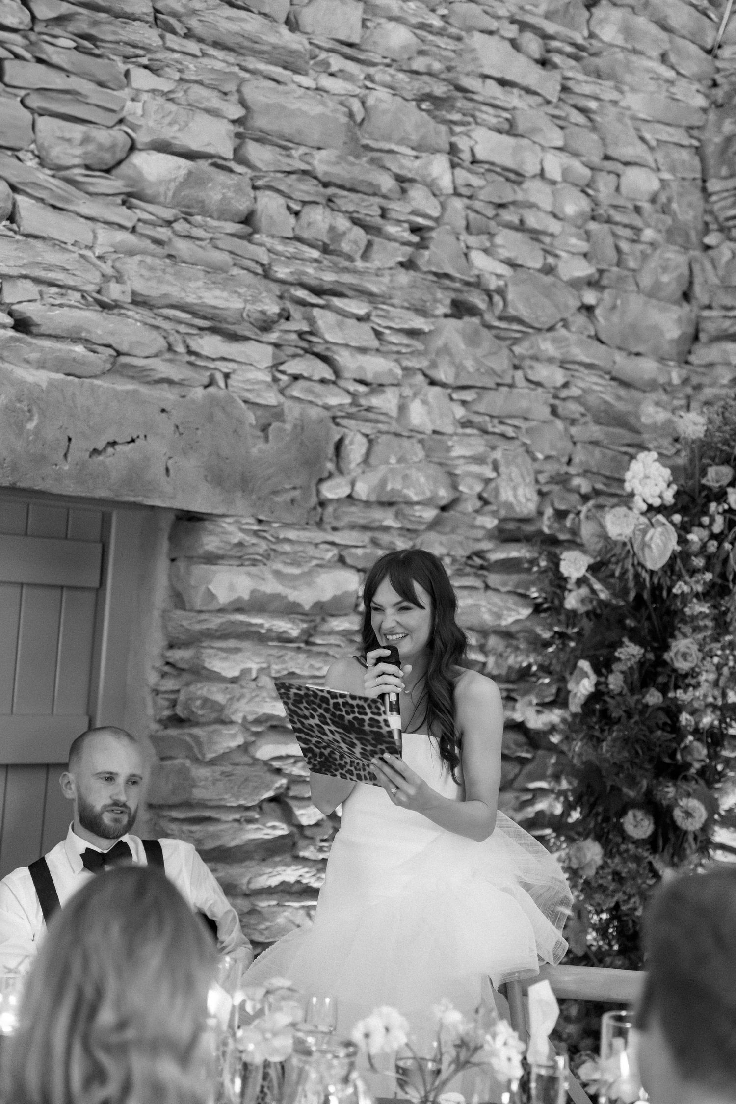 Formal dinner reception in a stone-walled venue with guests in black tie attire seated at decorated tables.