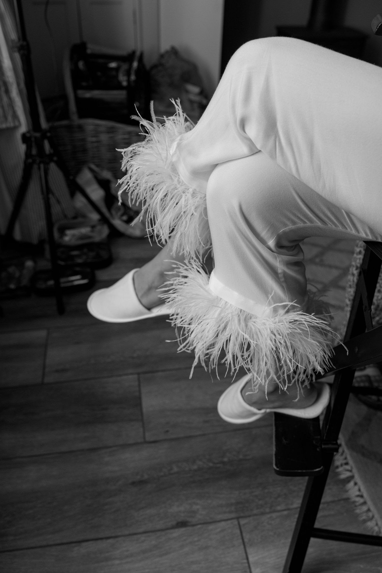 White feathered garment detail shown in black and white against wooden flooring.