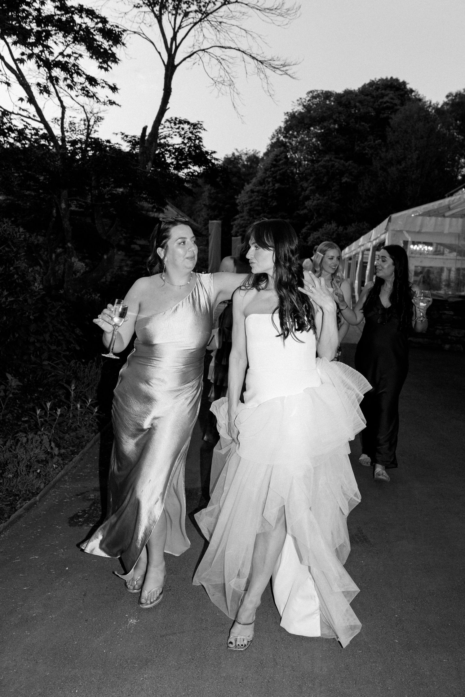 Wedding guests walk outside at dusk with trees in the background.