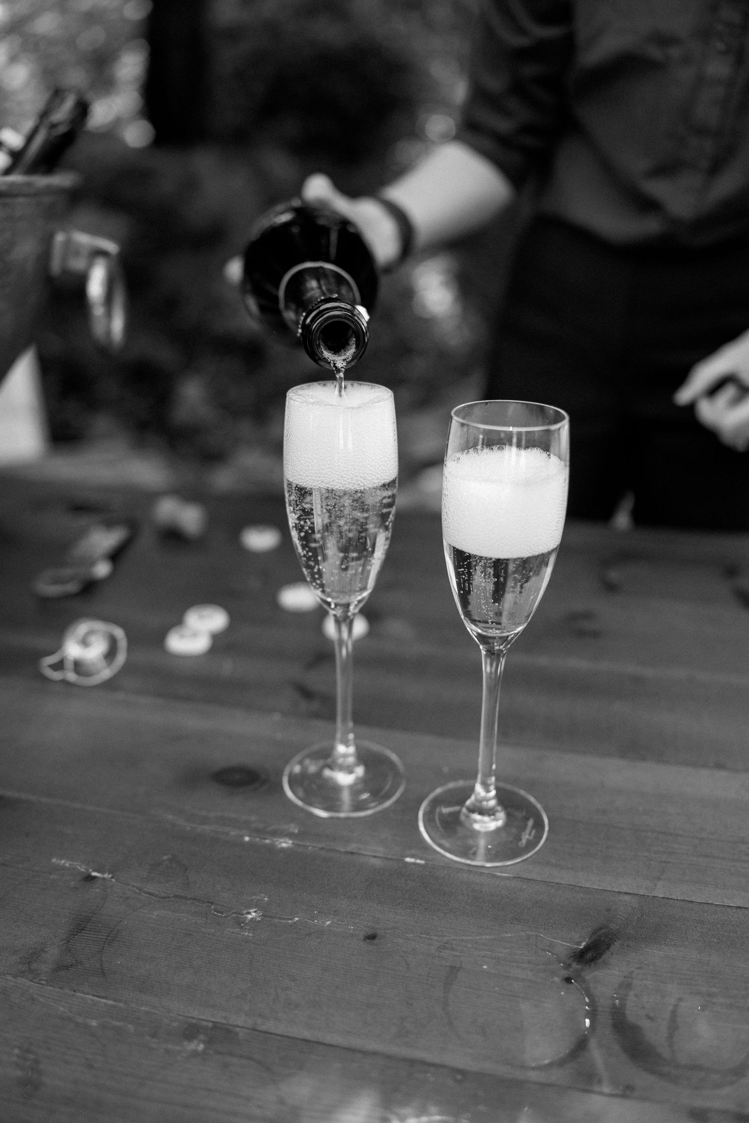 Black and white photo of champagne glasses and candles on a wooden table.