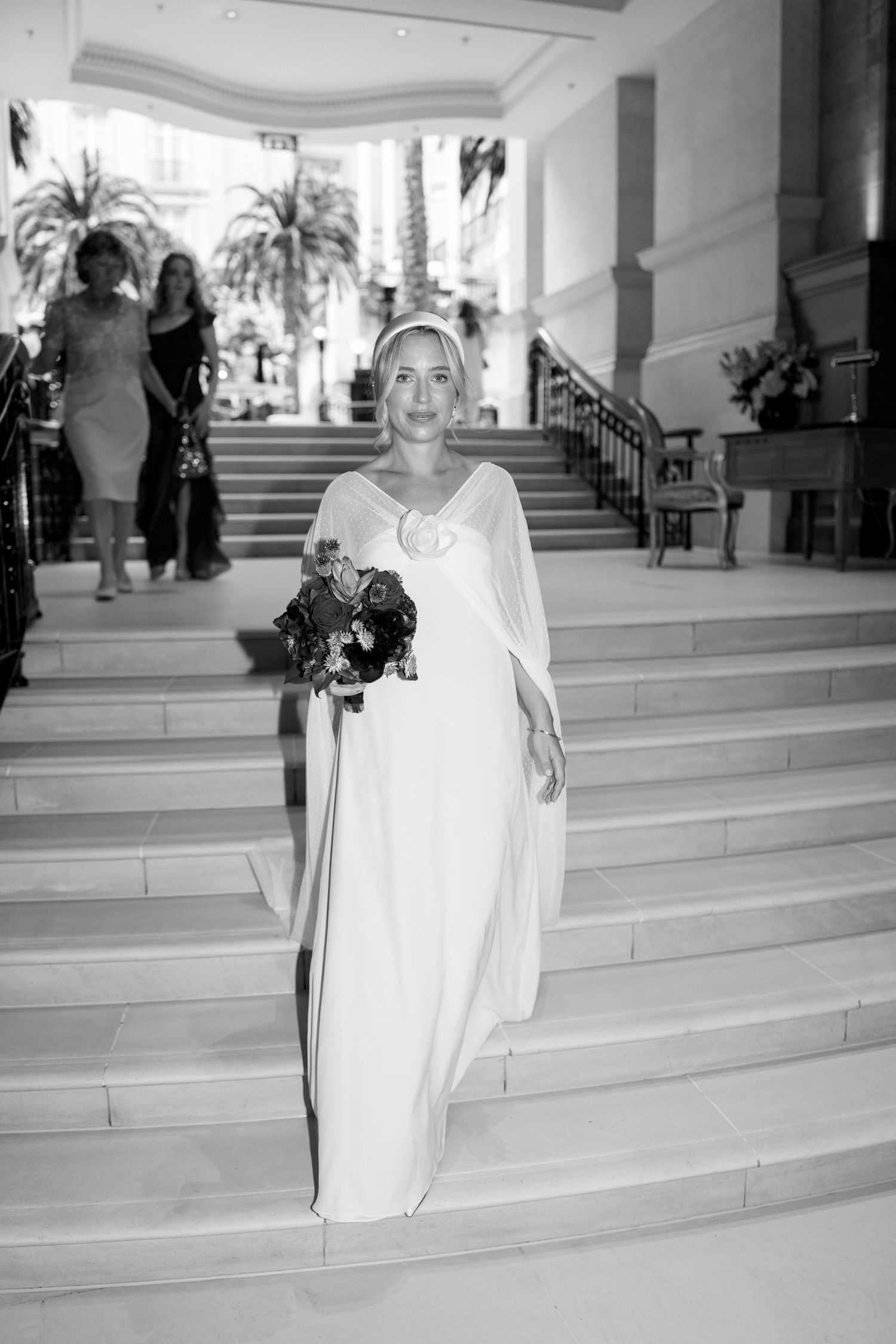 Black and white wedding photography capturing movement along grand marble stairs with decorative railings.