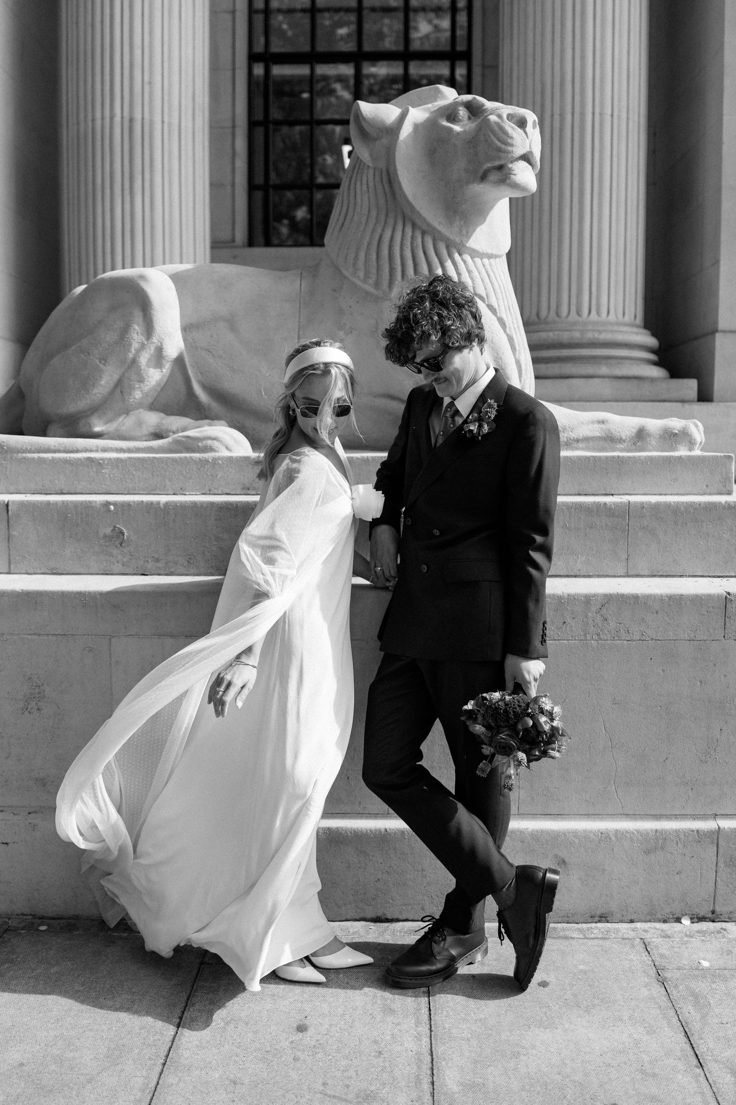 A wedding couple poses near classical stone columns and steps in black and white photography.