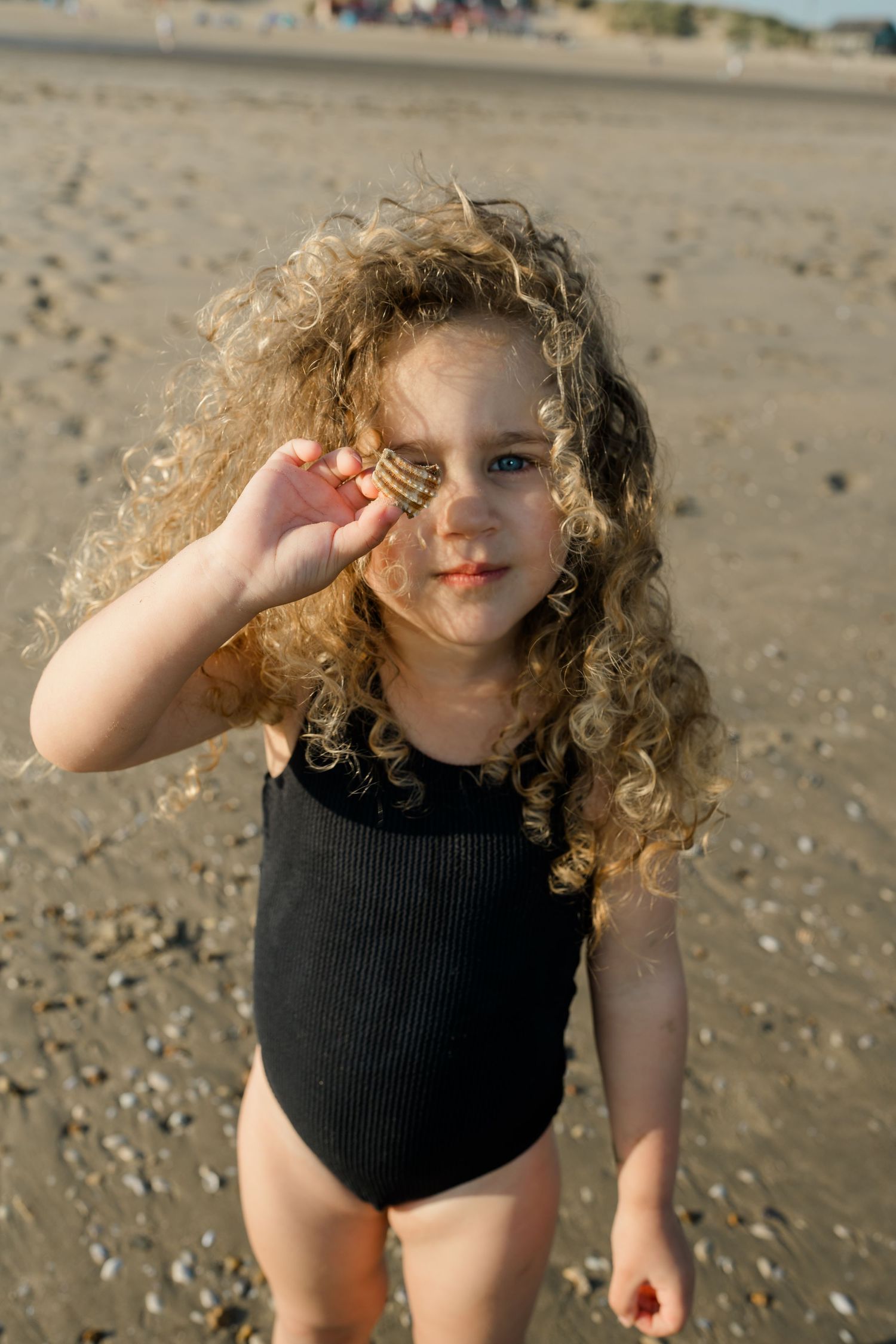 A child in a black swimsuit plays on a sandy beach on a sunny day.