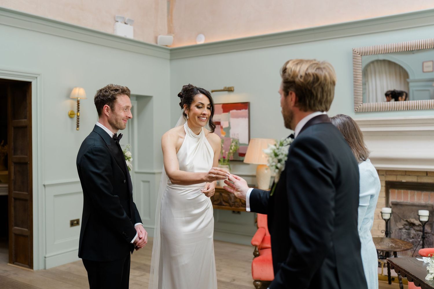 Bride and groom exchange rings during elegant indoor wedding ceremony with guests watching closely.