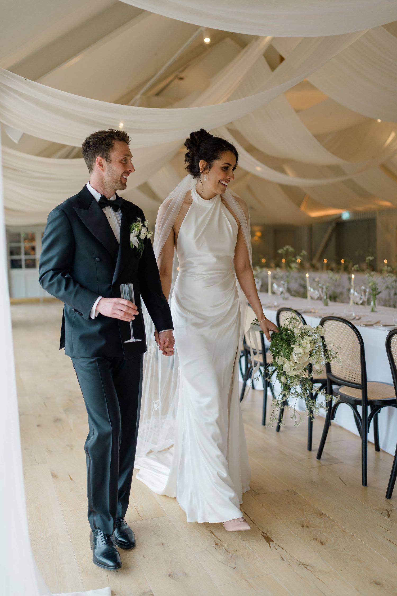 Bride and groom walking hand in hand through beautifully draped wedding reception venue.