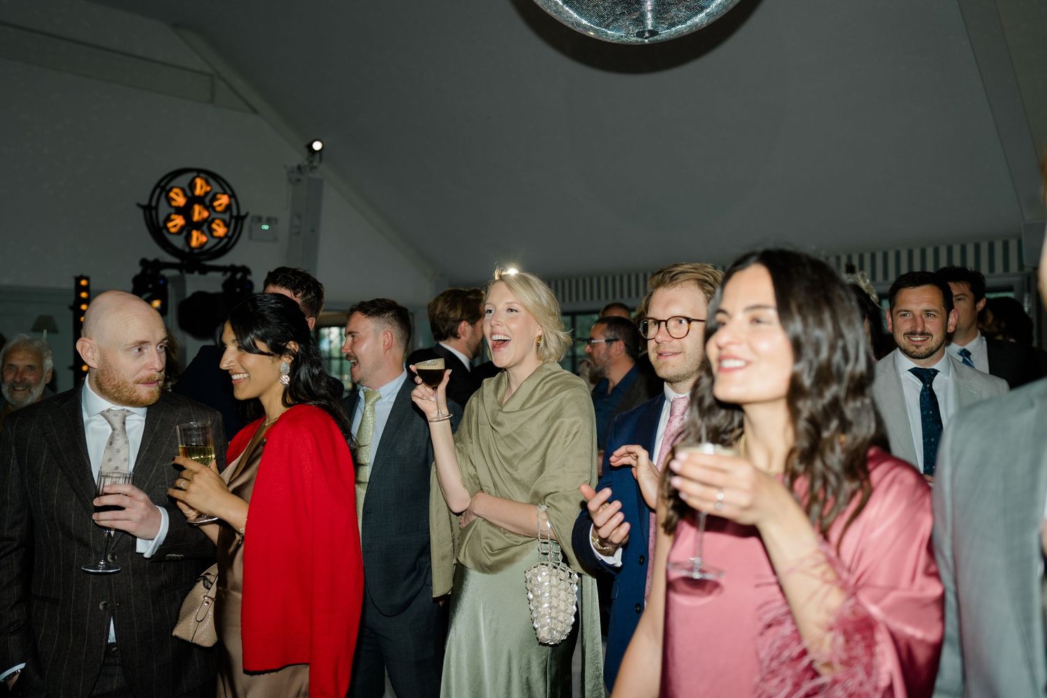 Elegant wedding cocktail hour with guests mingling and holding drinks under atmospheric lighting indoors.