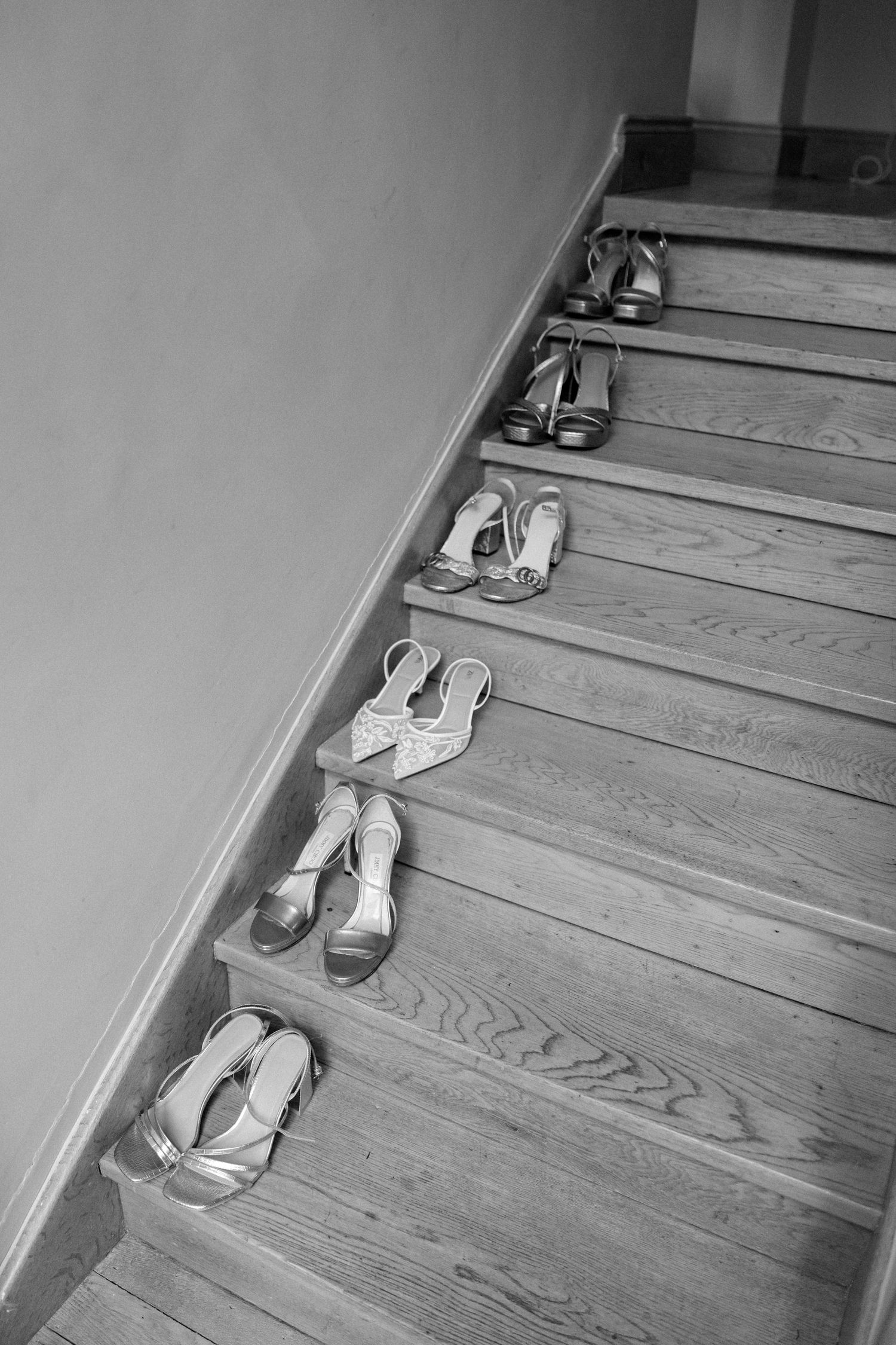 Wedding shoes arranged in ascending order on wooden stairs in black and white.