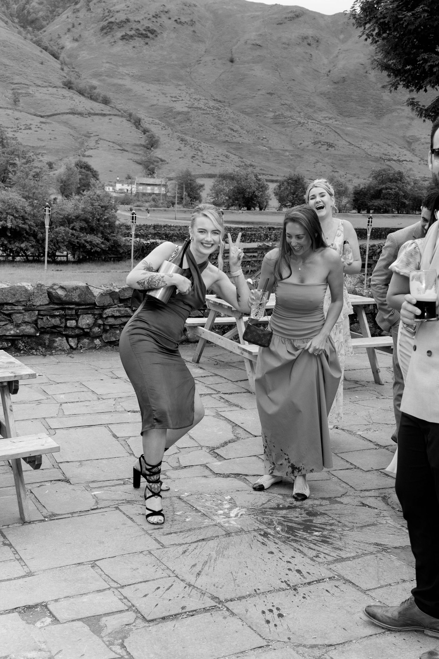 Wedding guests dance and pose on a stone patio with mountains visible in the distance.