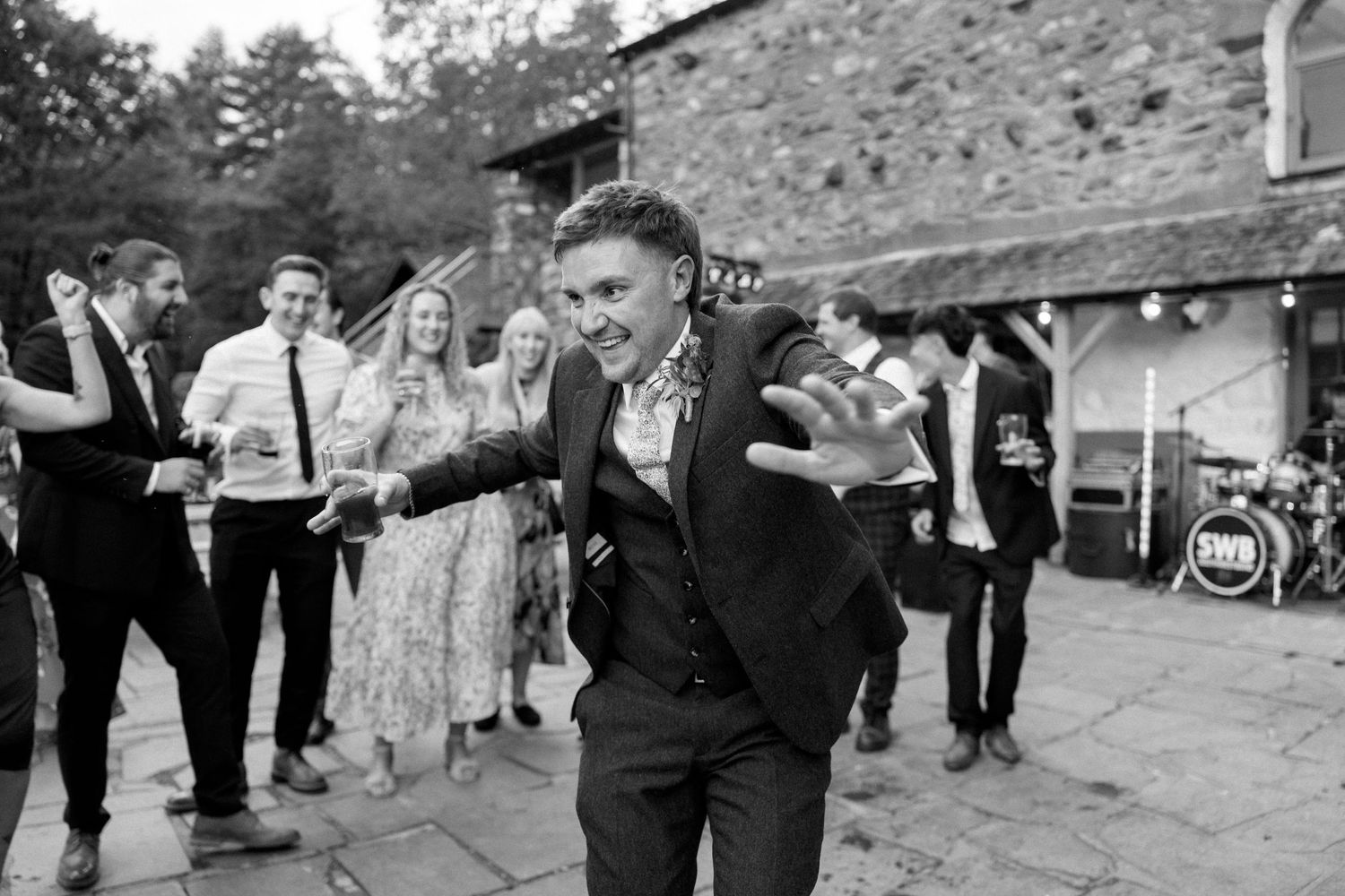 Guests dancing and celebrating at outdoor wedding reception with stone building backdrop.