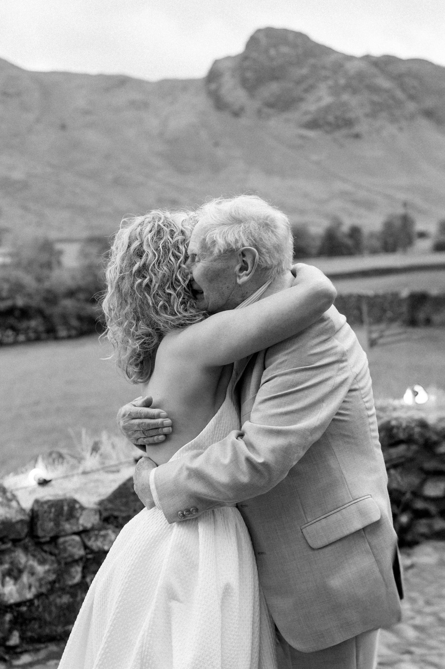 A couple embraces in an intimate black and white moment against a mountainous landscape backdrop.