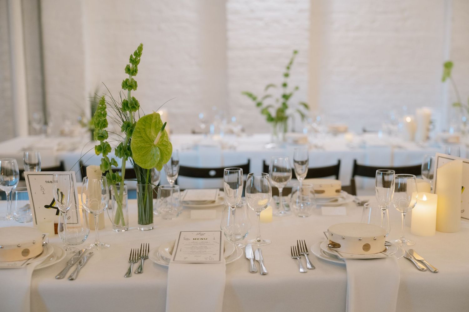 Minimalist wedding reception table settings with simple greenery centerpieces and white linens.