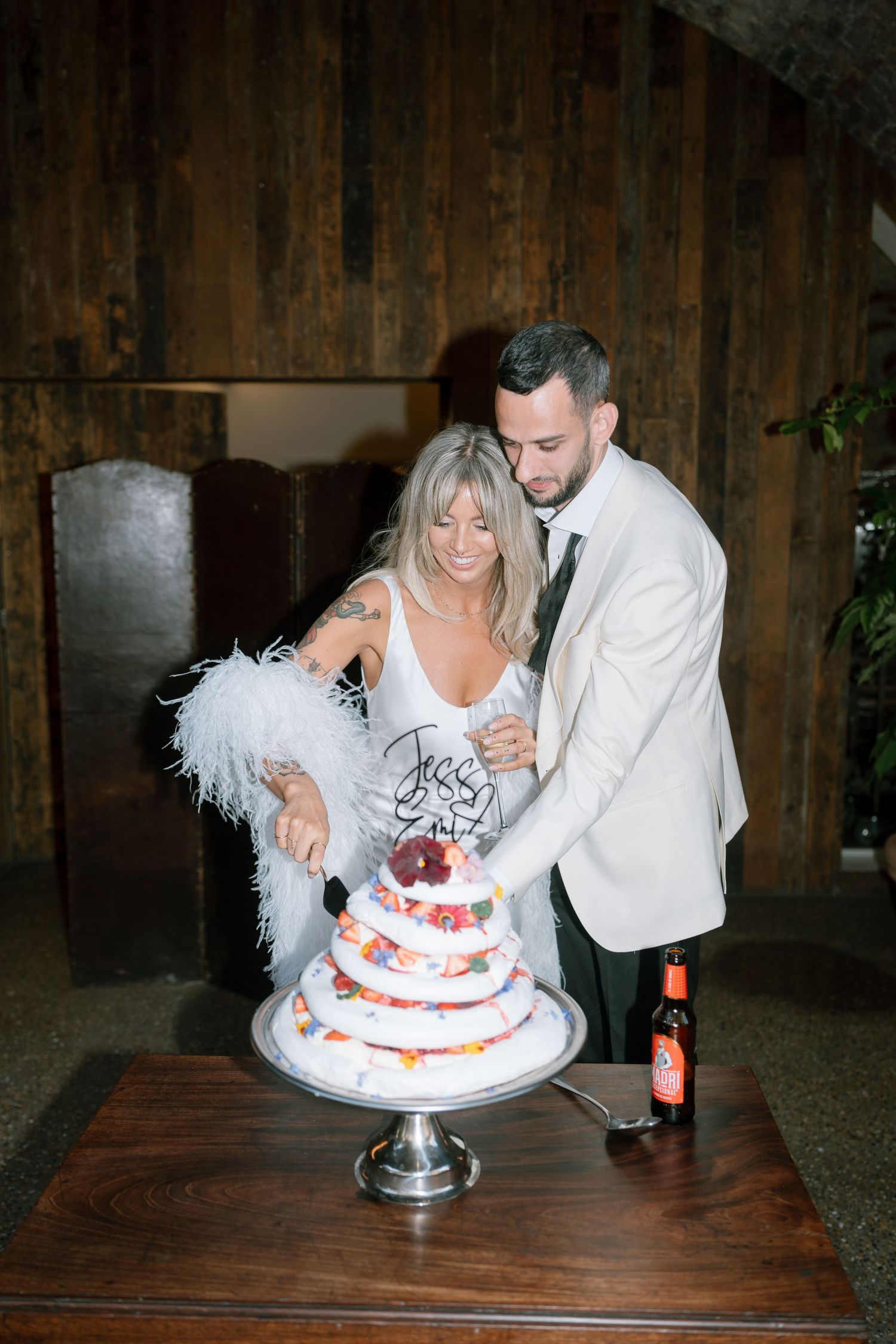 Wedding couple cutting into a white tiered cake decorated with fresh berries.