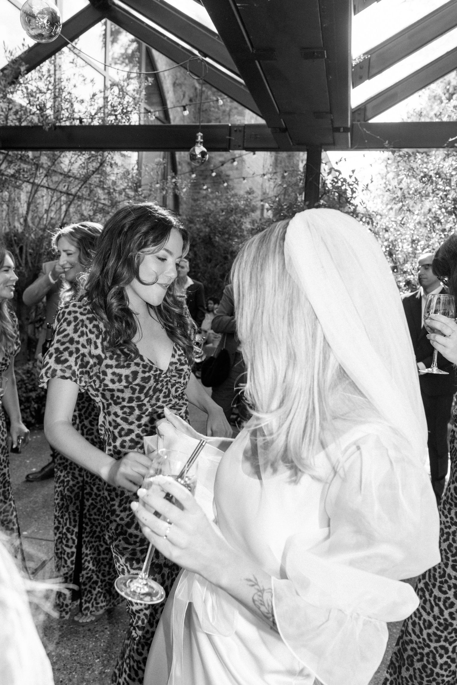 Black and white photo of wedding guests mingling and holding drinks at an outdoor reception.