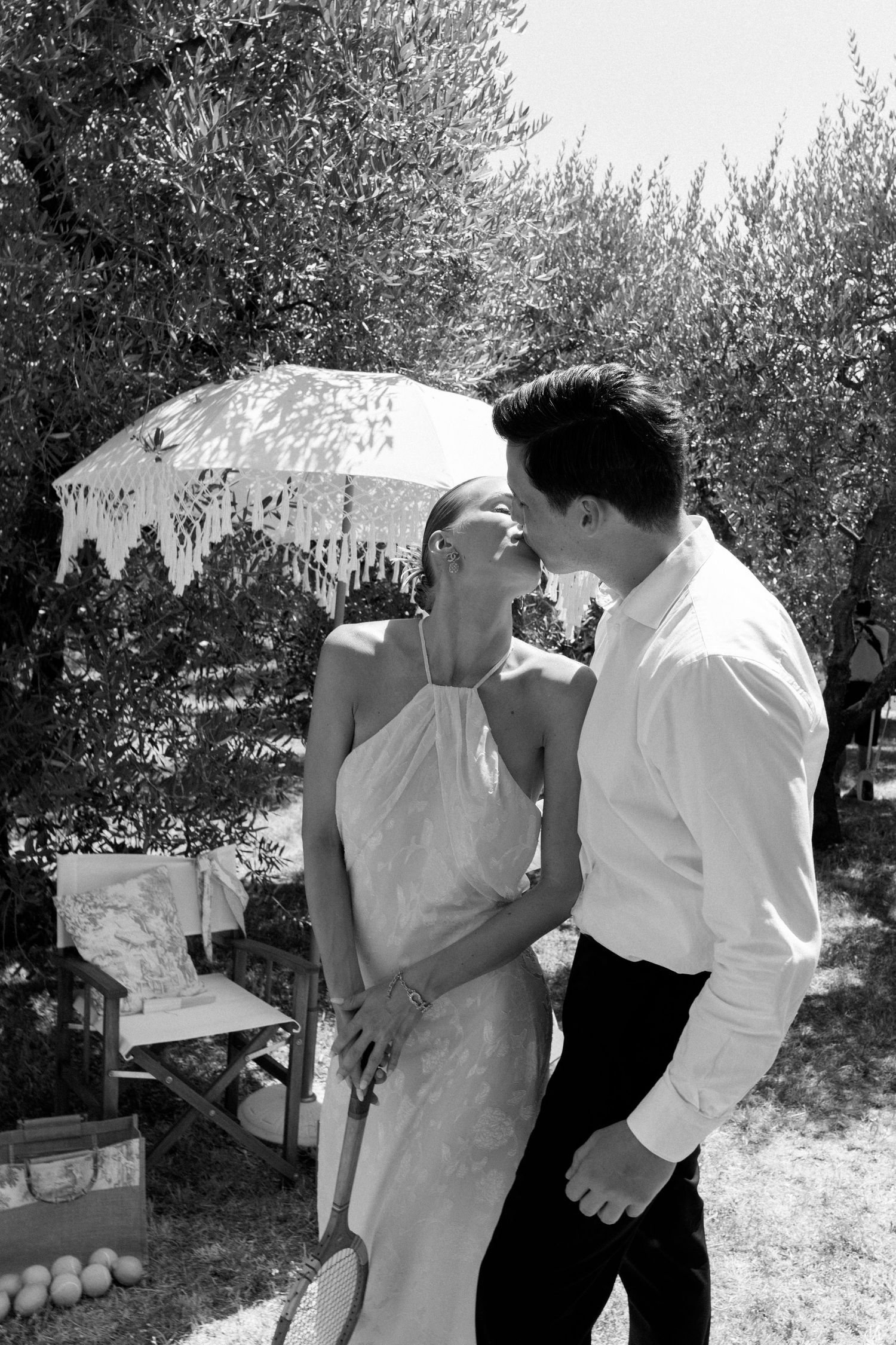 A romantic moment under a white parasol in an outdoor garden setting.