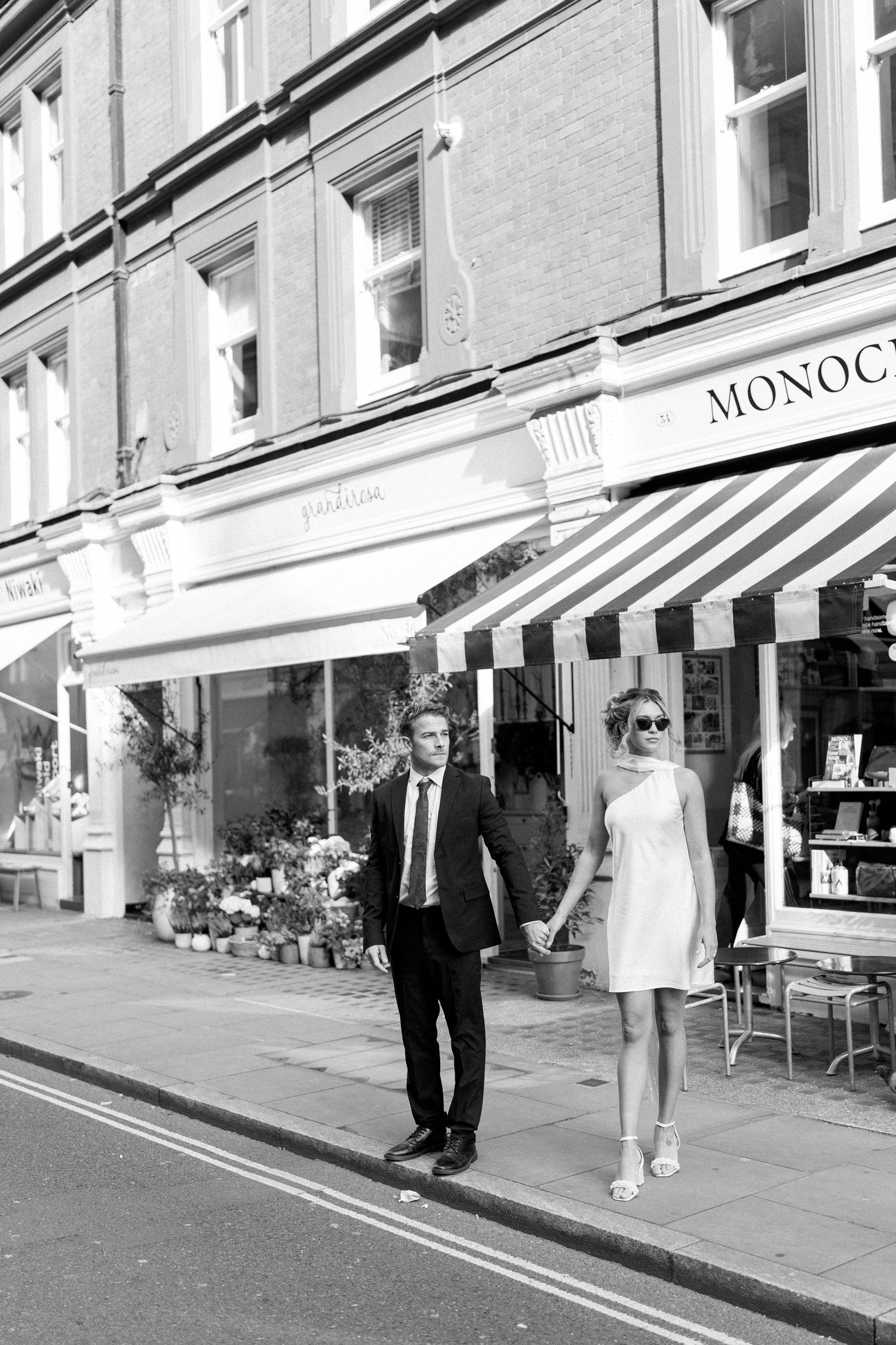 A couple walks together on a city street lined with storefronts and awnings.